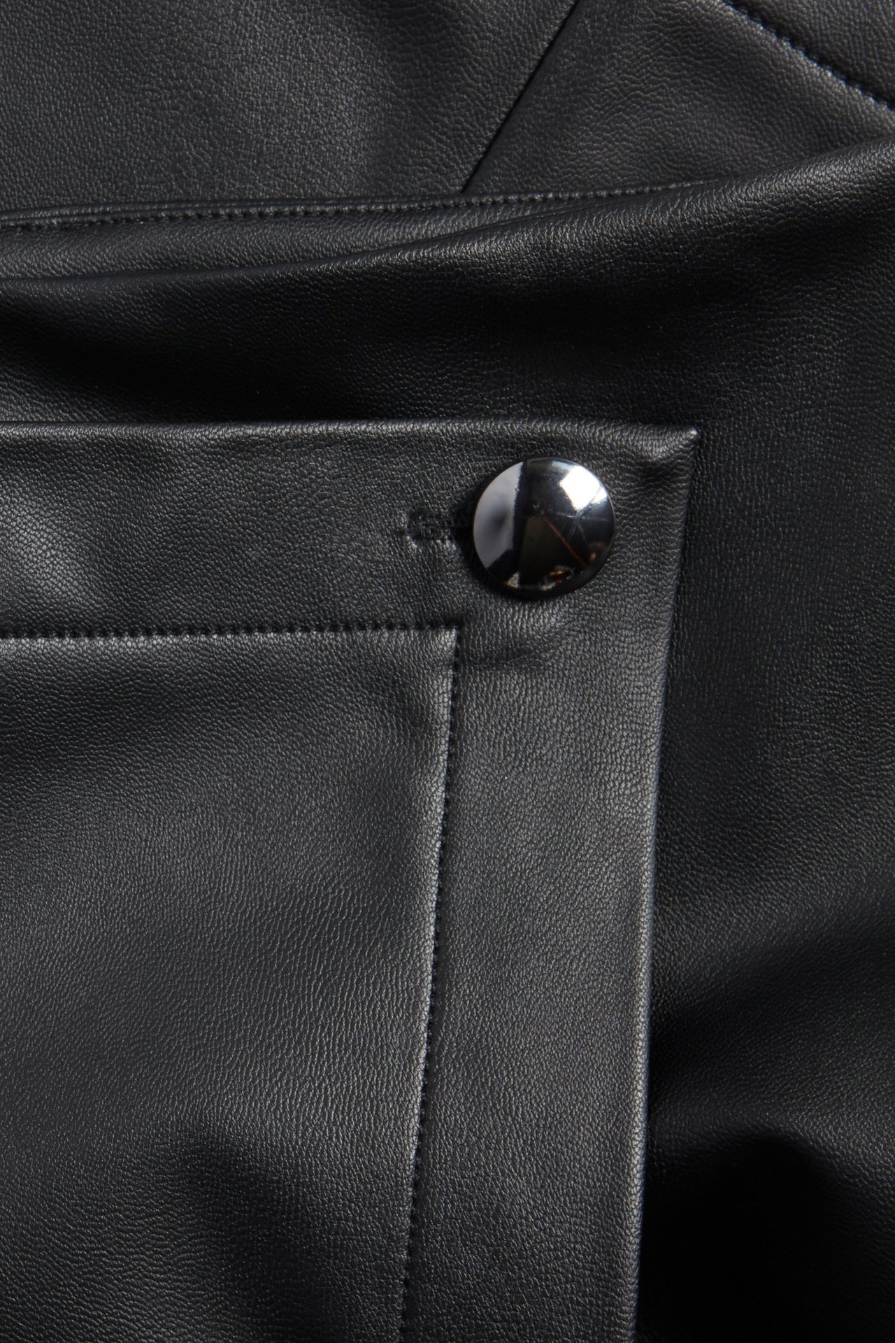 Zbliżenie czarnej spódnicy kopertowej ze sztucznej skóry ze srebrnym guzikiem.