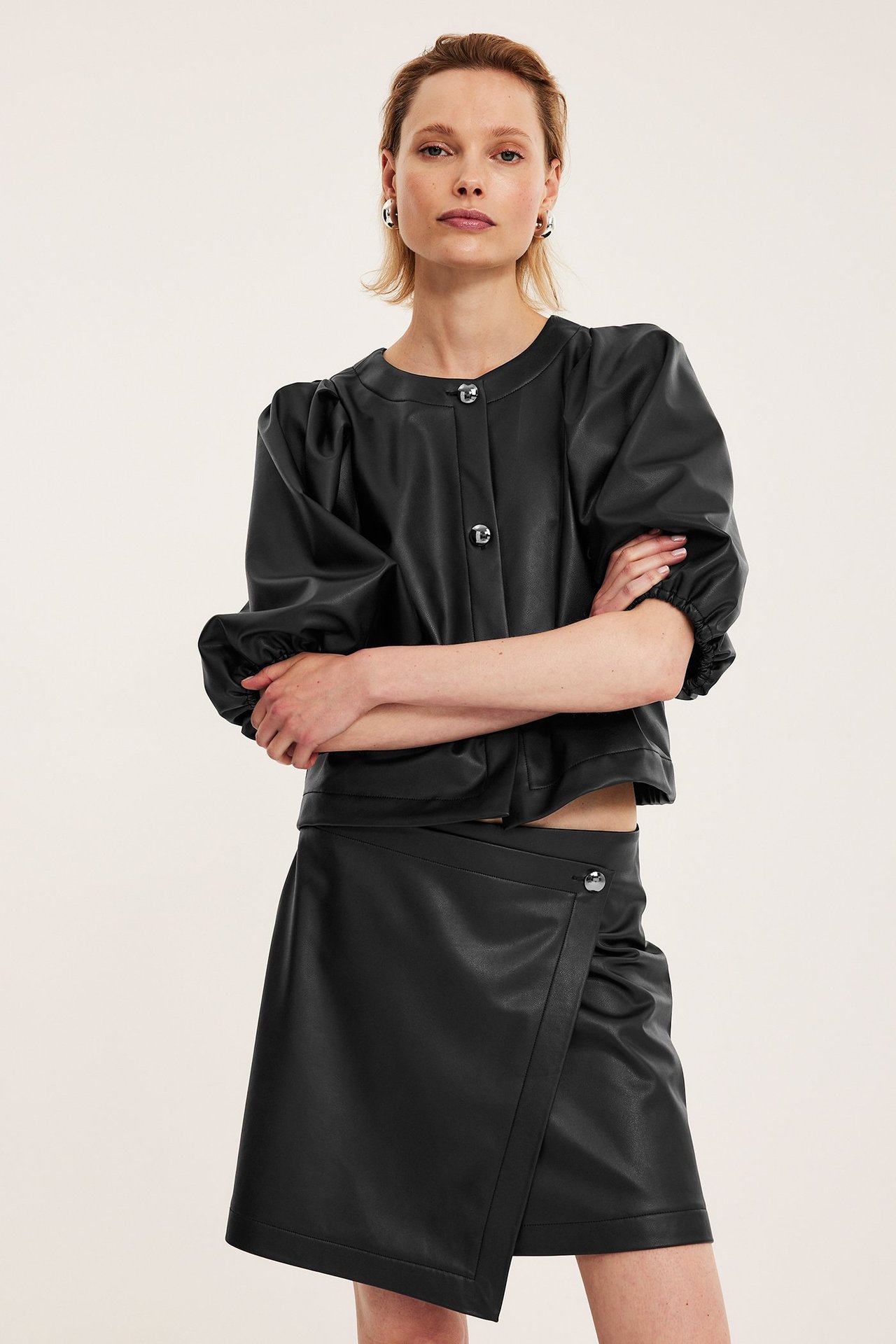 Edestä, nainen mustassa tekonahkaisessa kietauluhameessa napilla ja mustassa lyhyessä topissa.