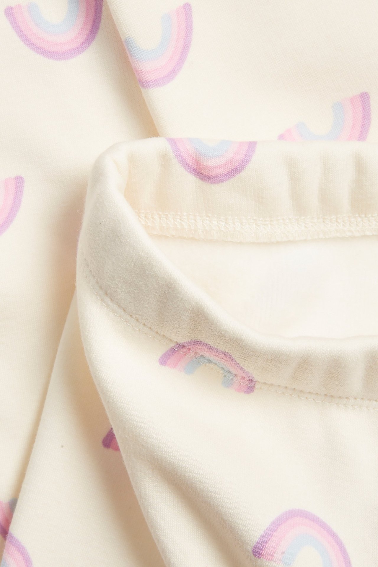 Zbliżenie na kremowe, ocieplane legginsy dziecięce z pastelowym wzorem tęczy.
