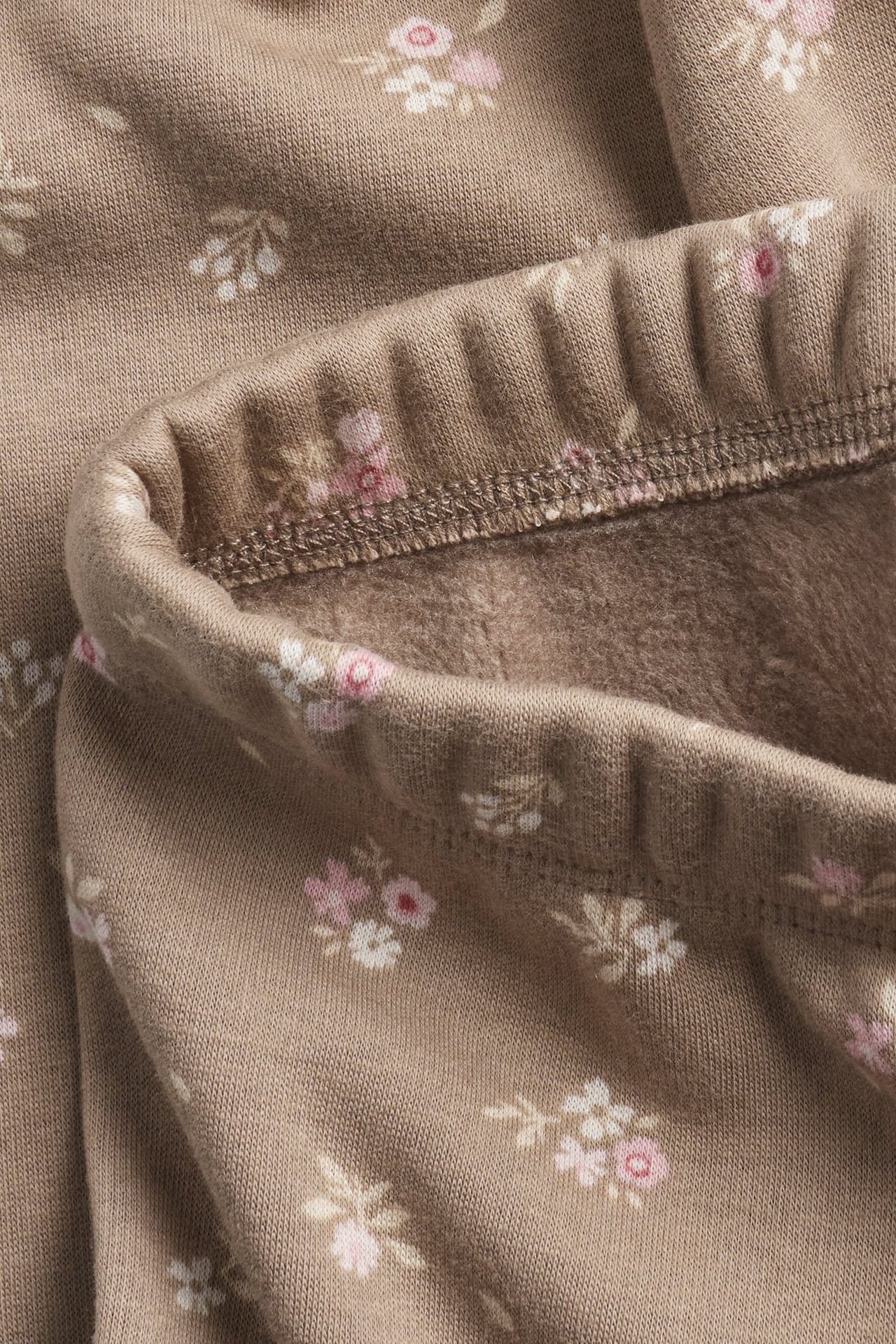 Zbliżenie beżowych, kwiecistych, ocieplanych legginsów z miękkim, szczotkowanym wnętrzem.