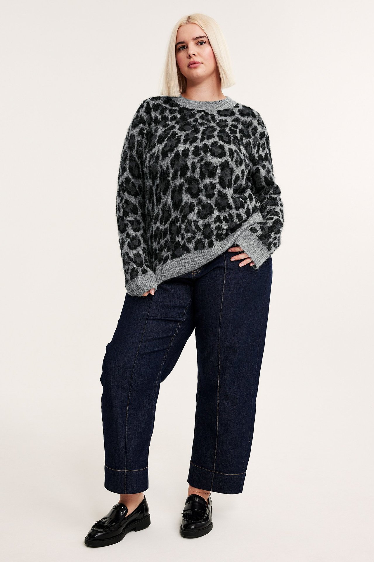 Edestäpäin: nainen yllään harmaameleerattu jacquard-neulepusero leopardikuviolla, tummansiniset farkut ja mustat loaferit.