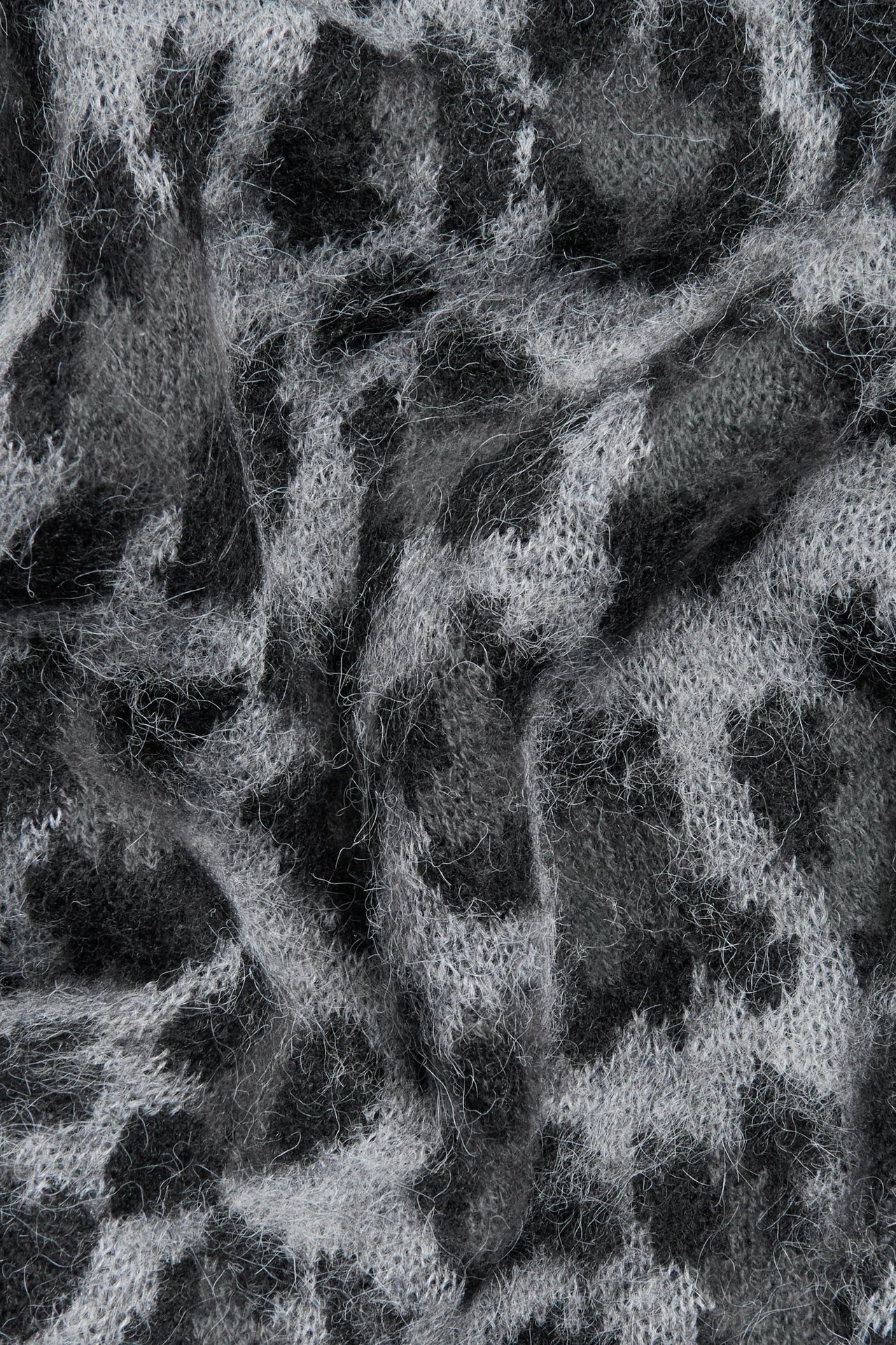 Zbliżenie szarego melanżowego swetra żakardowego z puszystym wzorem w panterkę.