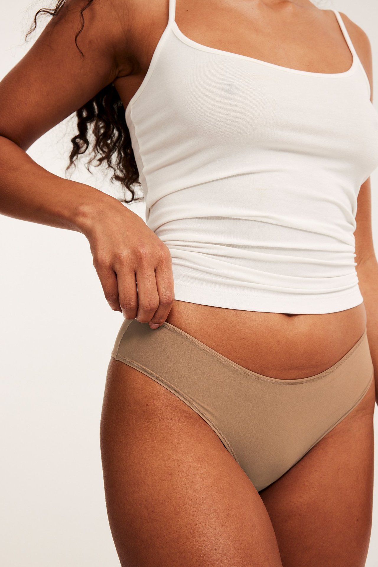 Nærbilde forfra av en kvinne i brune brazilian-truser og en hvit singlet.