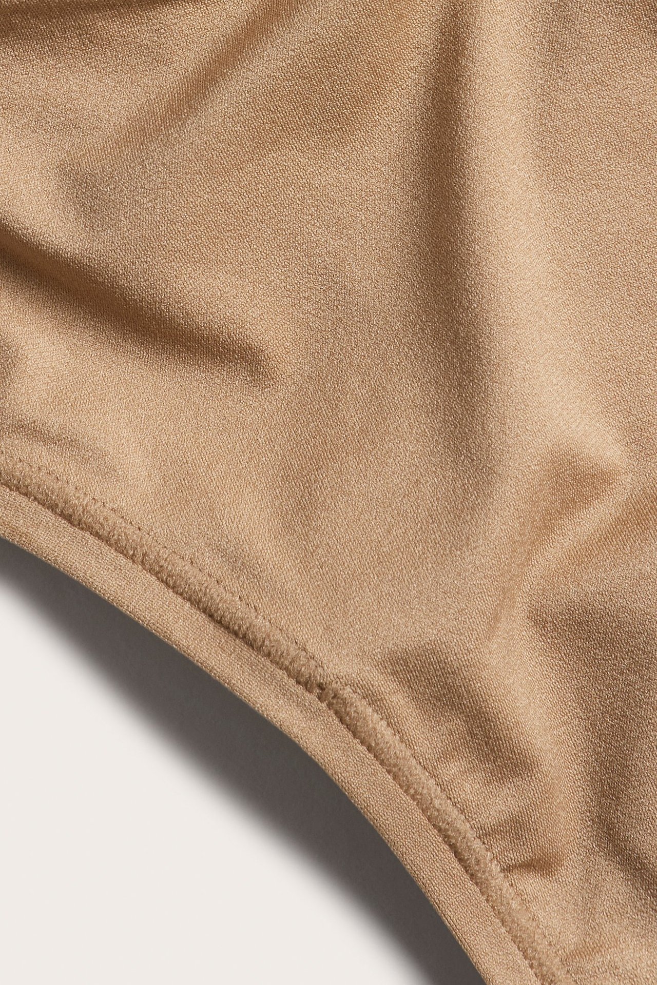 Zbliżenie na brązowe, jednolite, cienkie, elastyczne stringi z widocznym szwem.