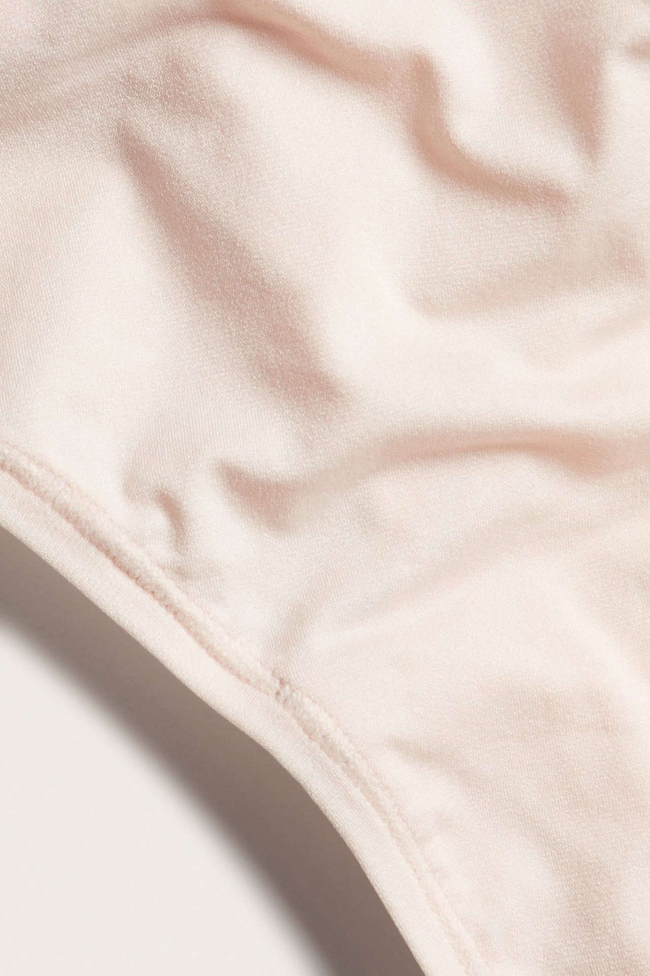 Zbliżenie jasnoróżowych, supermiękkich i cienkich stringów z elastycznego materiału ze szwami.