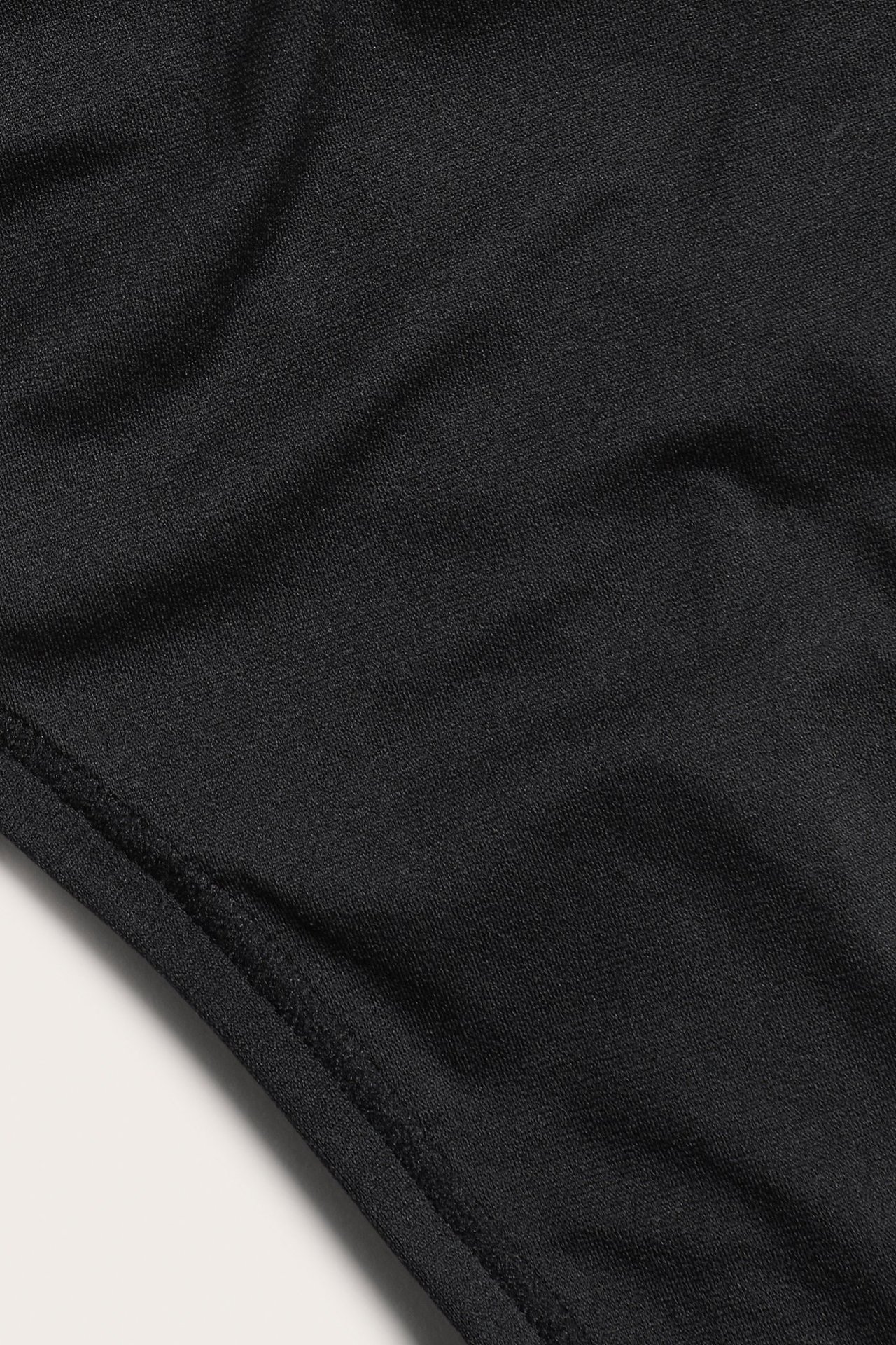 Zbliżenie na czarny, jednolity, rozciągliwy materiał z widocznymi szwami, na cienkie stringi.