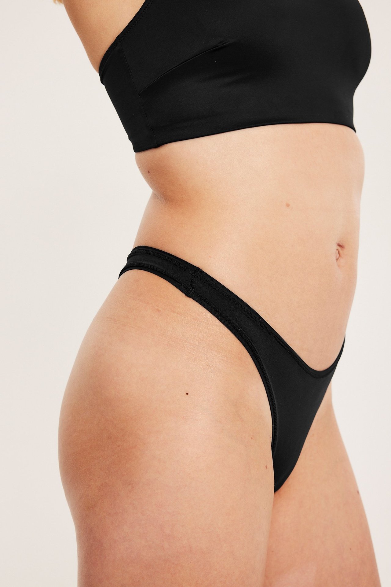 Sidebilde av en kvinne i svart tynn stringtruse og en svart bralette.