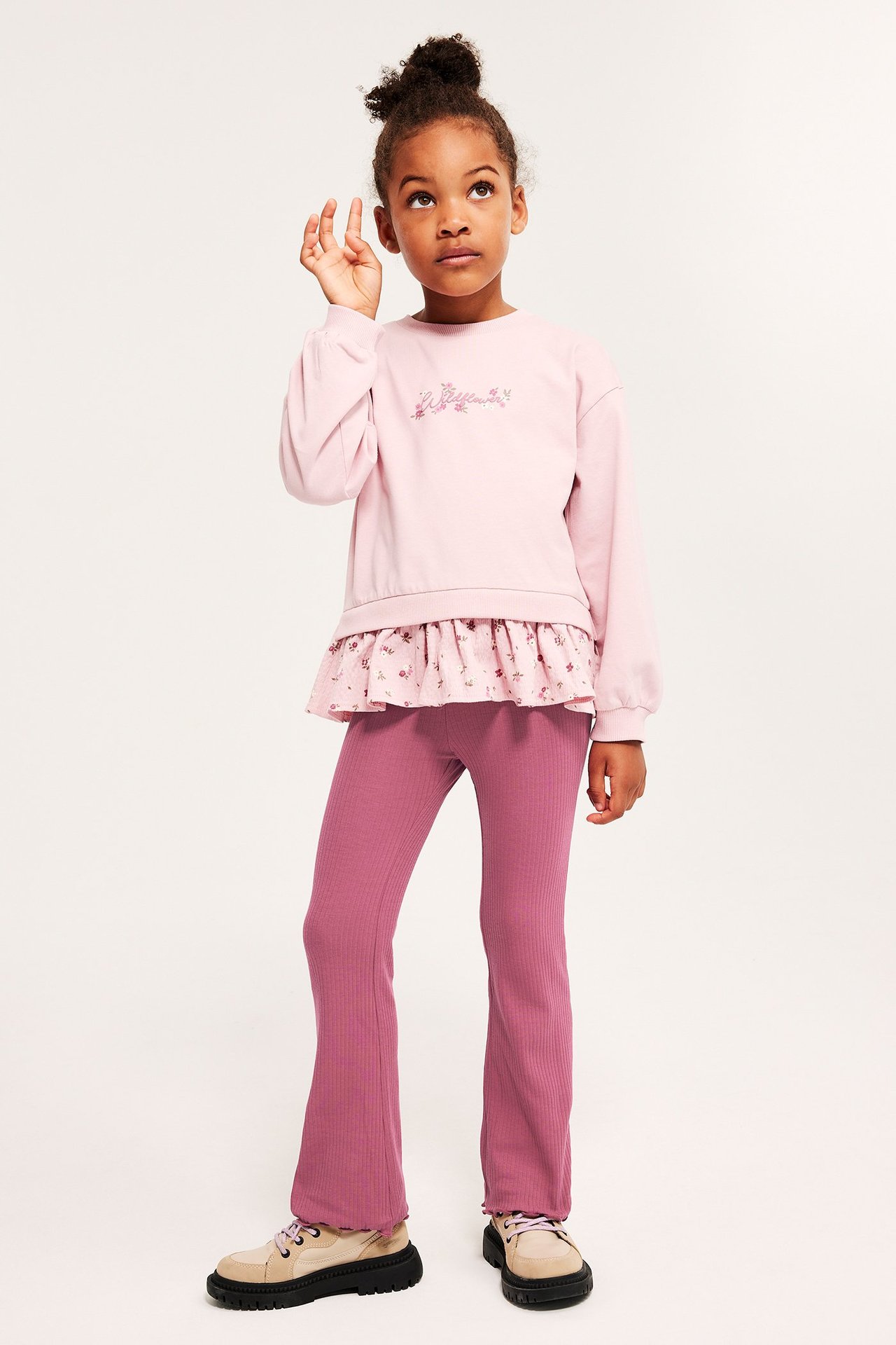 Edestä: Lapsi yllään tummanroosat ribatut flare-leggingsit, vaaleanpunainen toppi ja beiget kengät.