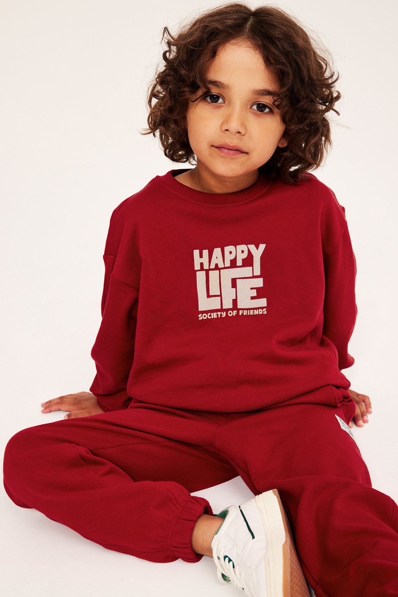 Frontvy av ett barn i röd bomullssweatshirt med 'HAPPY LIFE' velourtryck och matchande röda mjukisbyxor.