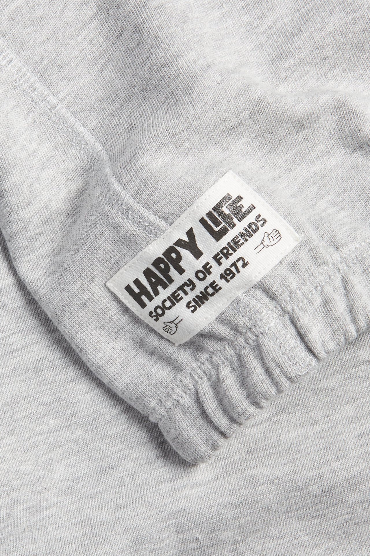 Zbliżenie na jasnoszarą bluzę z mieszanki bawełny z białą metką 'Happy Life' i ściągaczem.