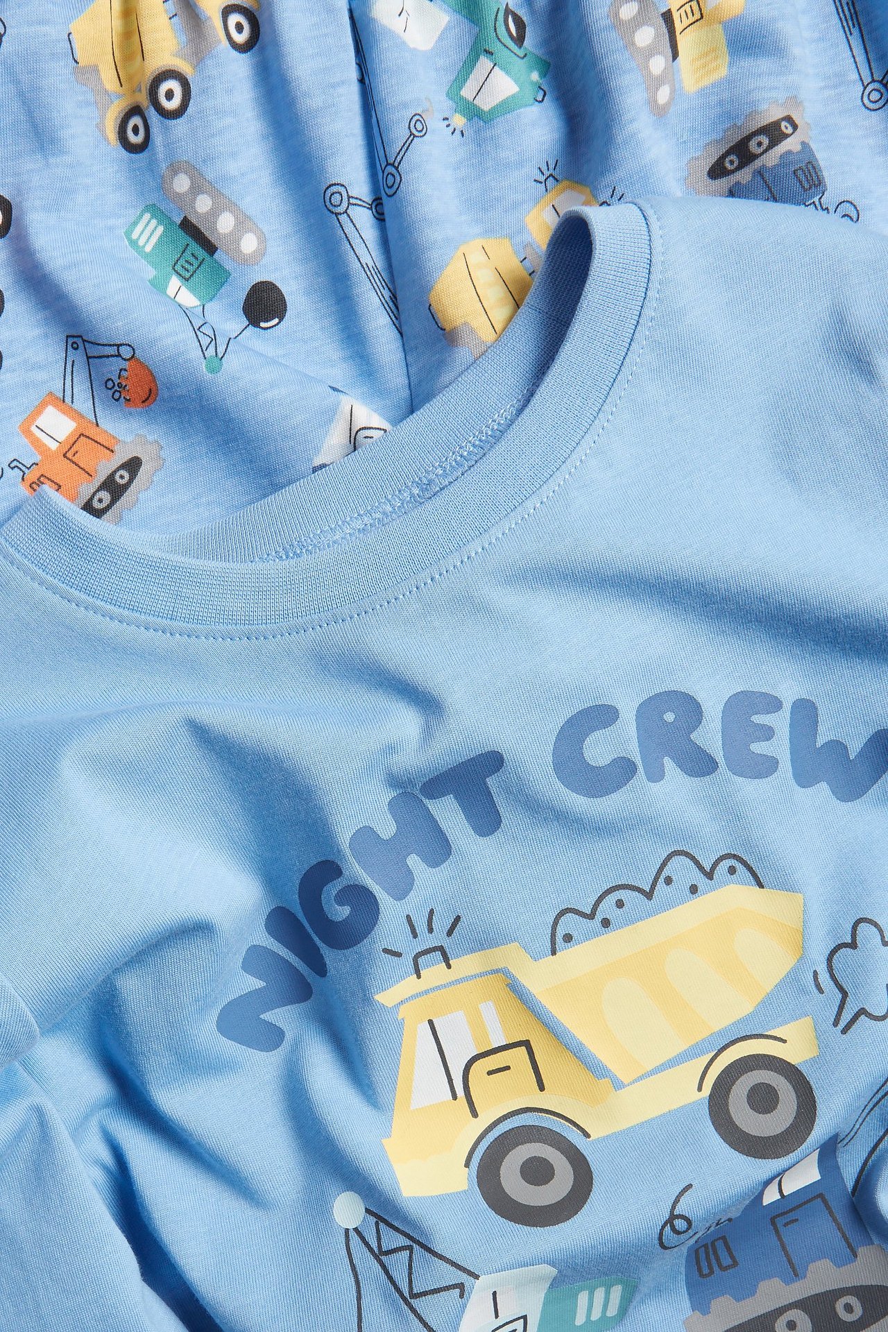 Lähikuva lapsen vaaleansinisestä puuvillapyjamasetistä, jossa ajoneuvoprintti ja "NIGHT CREW" -teksti.