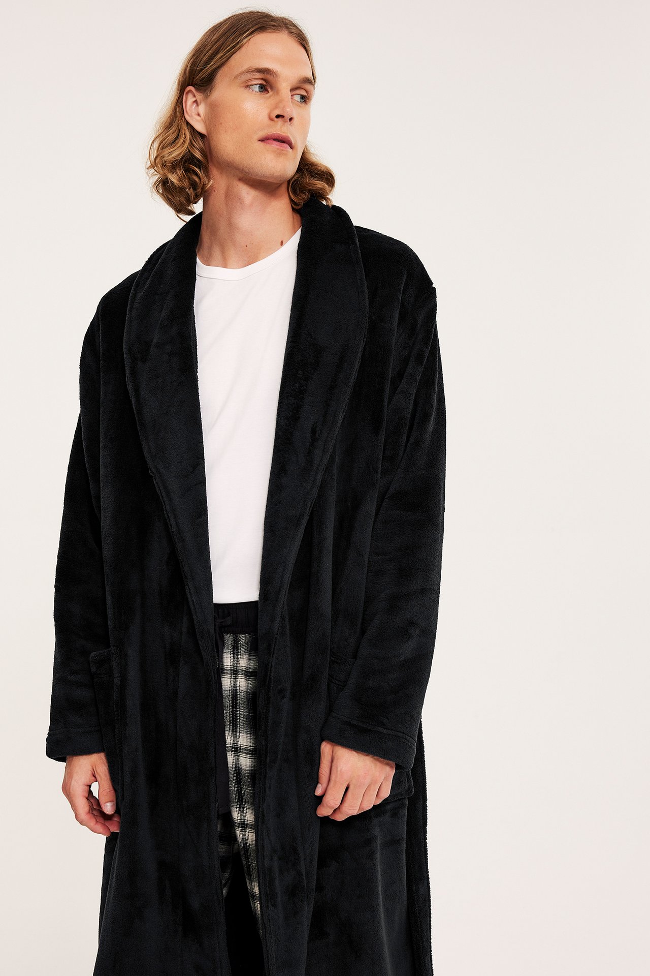 Frontvisning av en mann i svart fleece morgenkåpe over hvit t-skjorte og rutete pyjamasbukser.
