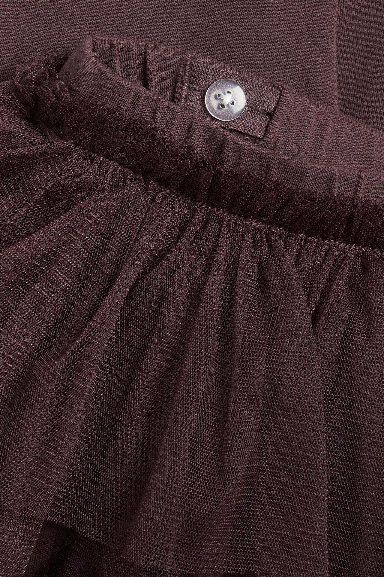 Zbliżenie na ciemnofioletowe bawełniane legginsy z doszytą falbaniastą spódniczką tiulową i guzikiem w pasie.