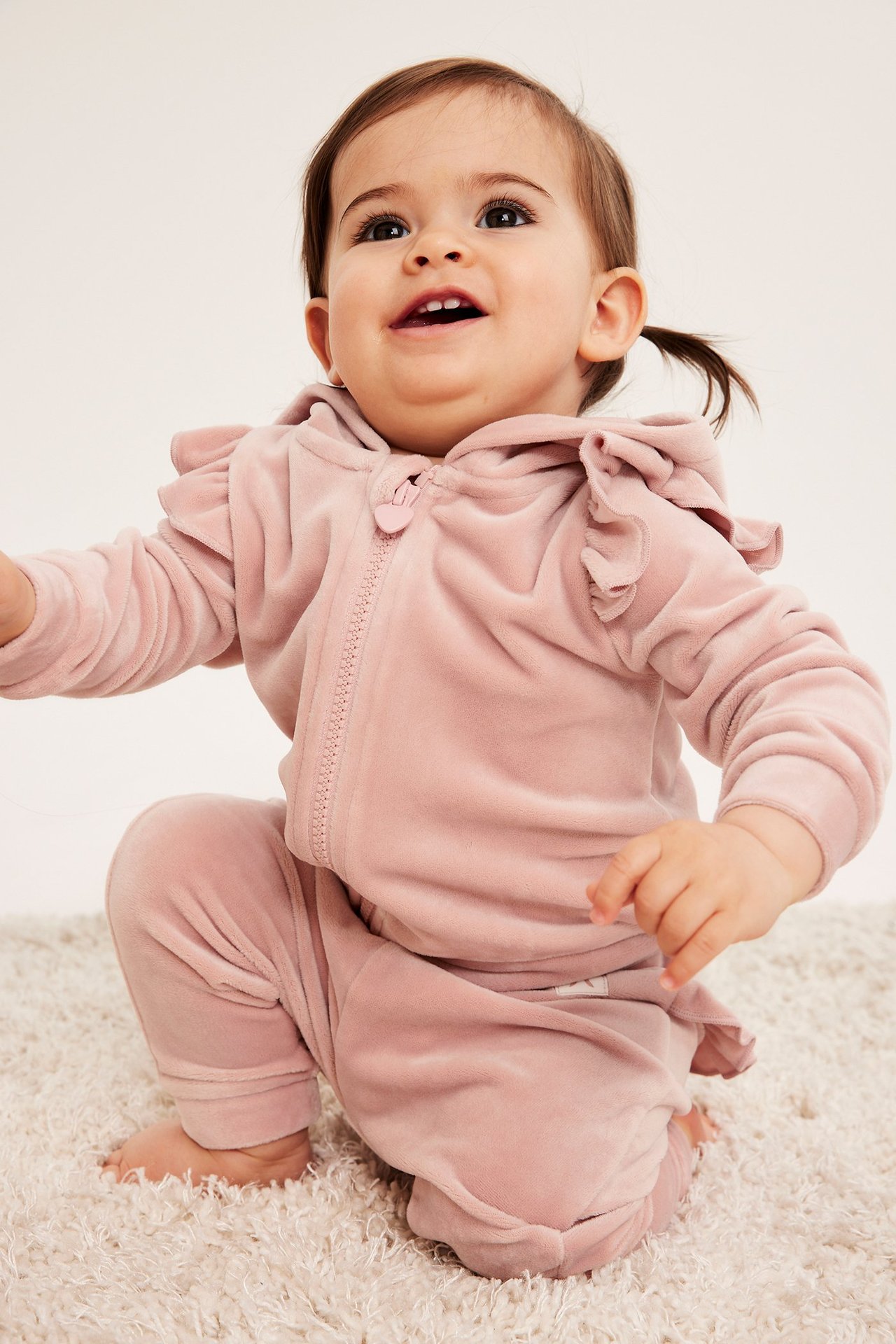 Forfra, baby i rosa velour hettegenser med volanger og matchende joggebukse.