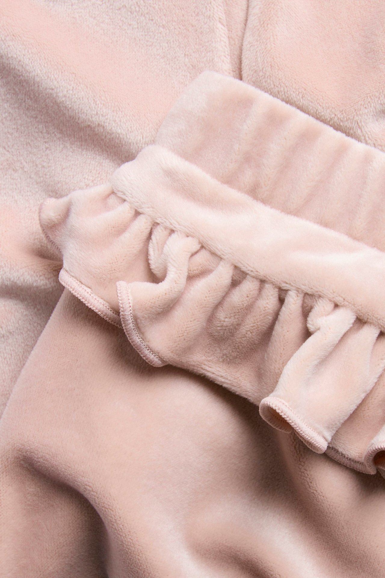 Zbliżenie różowych welurowych spodni dresowych z falbanką.