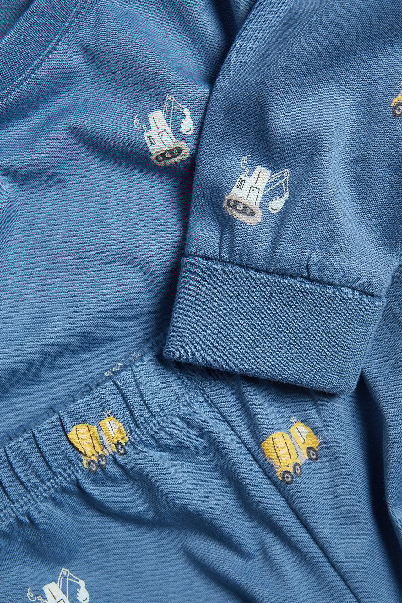 Lähikuva sinisistä puuvillaisista lasten pyjamista, joissa ajoneuvokuvio, resorit hihansuissa ja vyötäröllä.