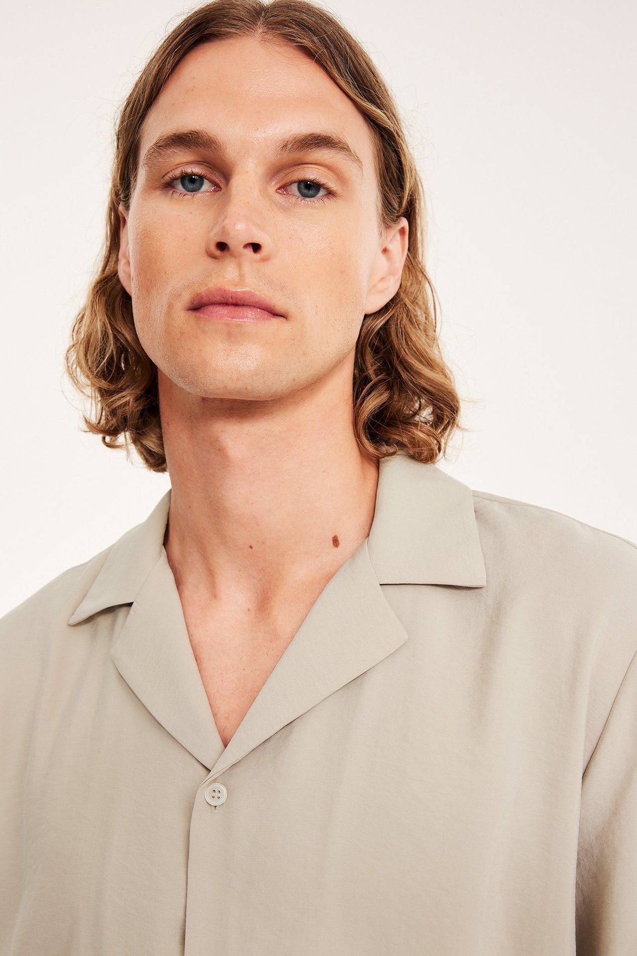 Lähikuva edestä miehestä, jolla on yksivärinen beige lyhythihainen resort-paita resort-kauluksella.