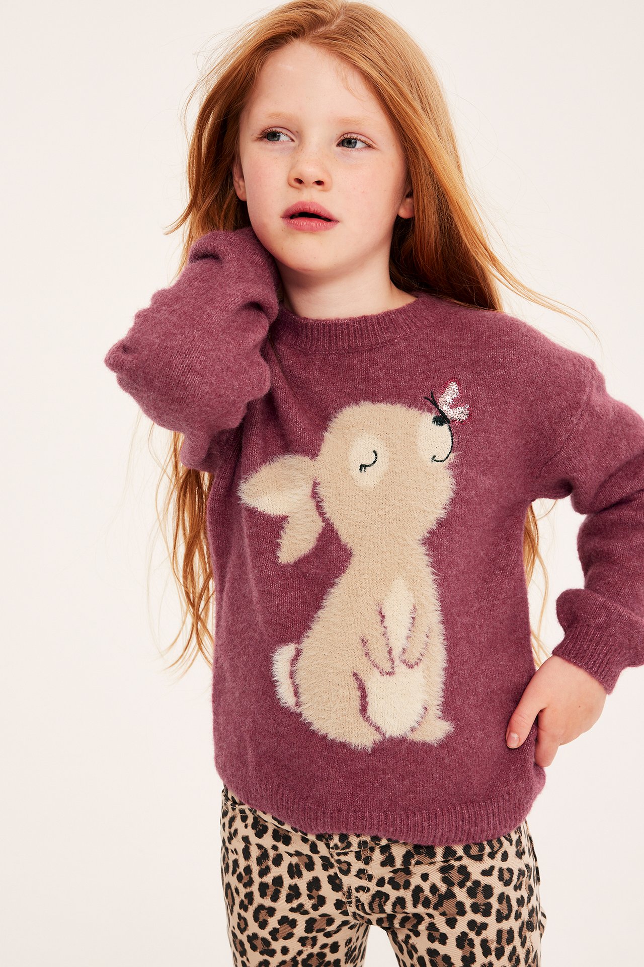 Frontvy av ett barn i en mörkrosa stickad tröja med fluffig beige kanin och leopardmönstrade leggings.