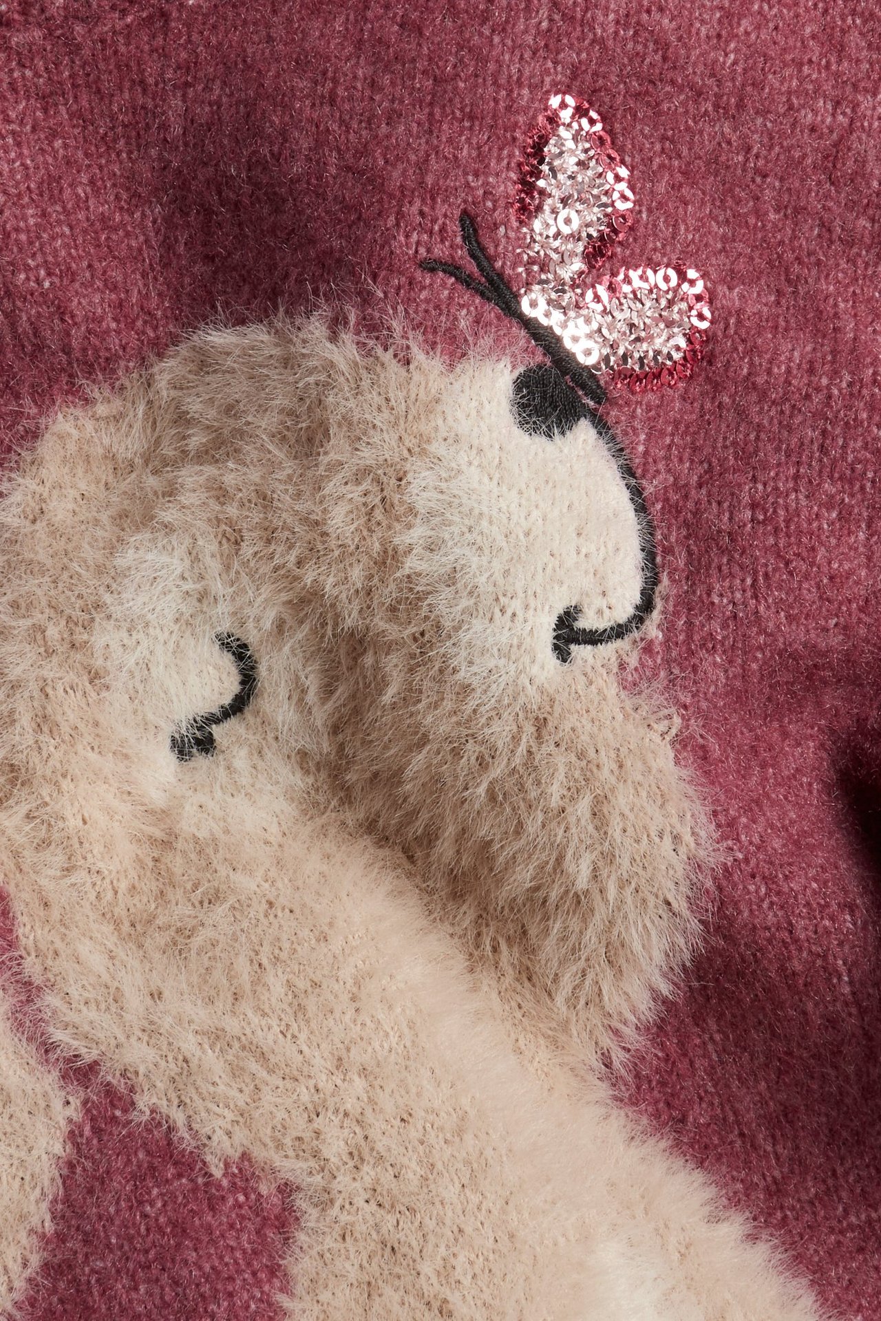 Zbliżenie na ciemnoróżowy sweter z dzianiny z puszystą beżową intarsją zwierzęcą i różową aplikacją motyla z cekinów.