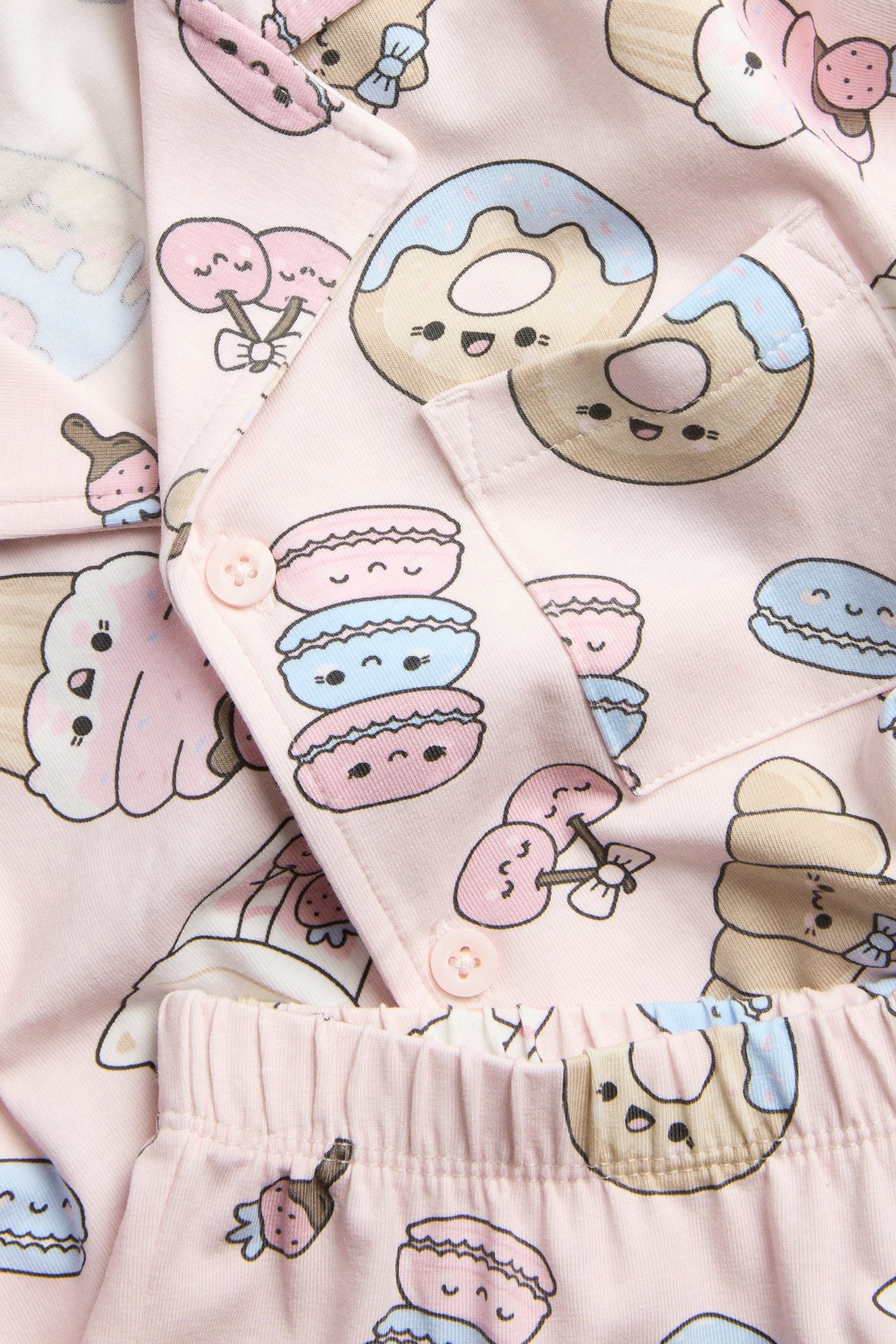 Lähikuva lasten vaaleanpunaisesta jersey-pyjamasta, jossa on jälkiruokakuvio, napit ja joustava vyötärö.