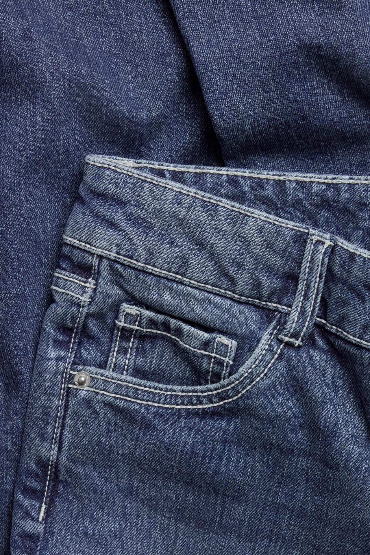 Zbliżenie na ciemnoniebieskie jeansy bootcut z białymi przeszyciami i małą przednią kieszenią.