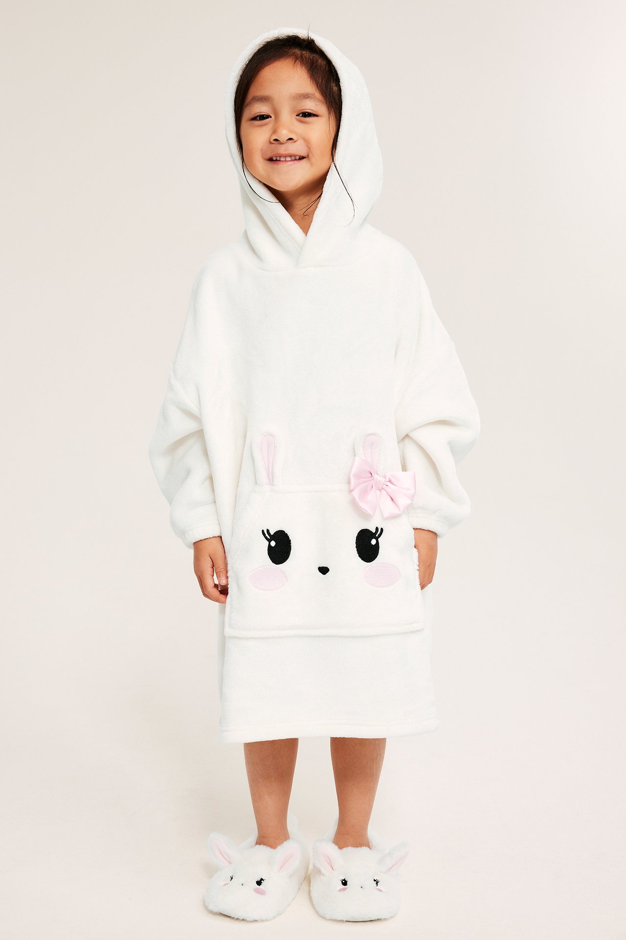 Jente i offwhite fleece-hoodie med kaninpåkningsbroderi, rosa sløyfe og kanin-slippers.