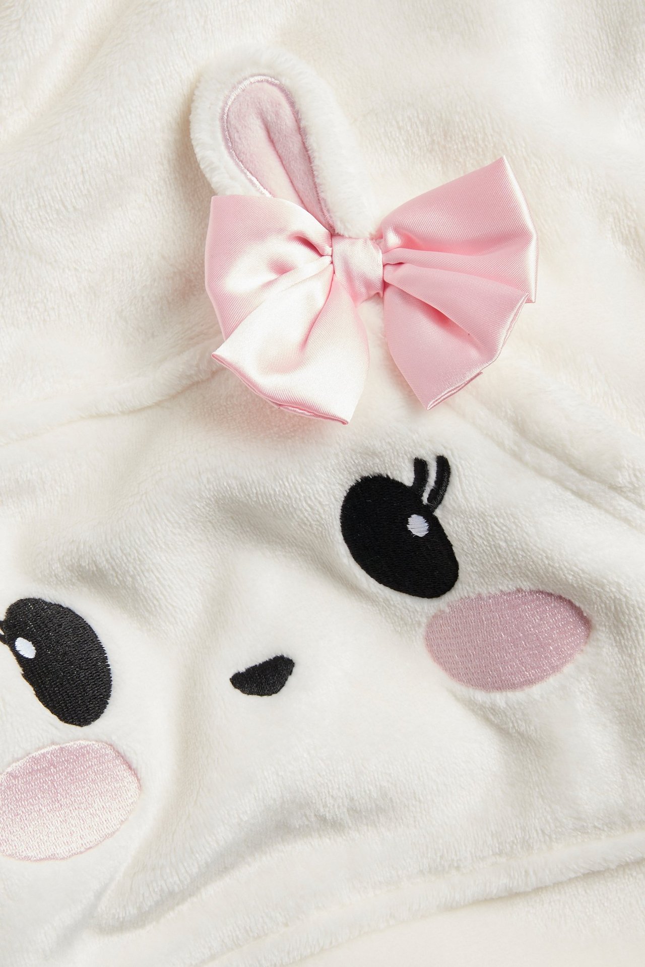 Zbliżenie na ecru dziecięcą bluzę polarową z różową kokardą, uszami królika i haftowaną buźką.