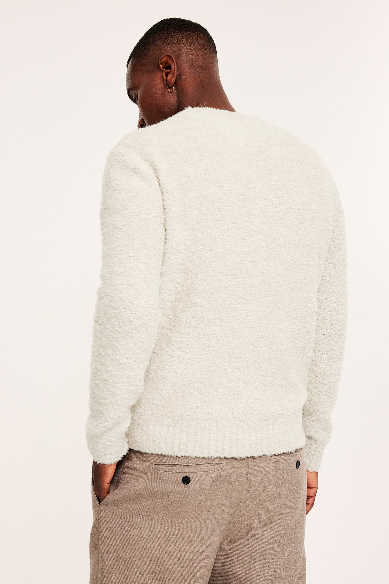 Bakfra: Mann i beige O-hals genser i bouclé-strikk og brune bukser.