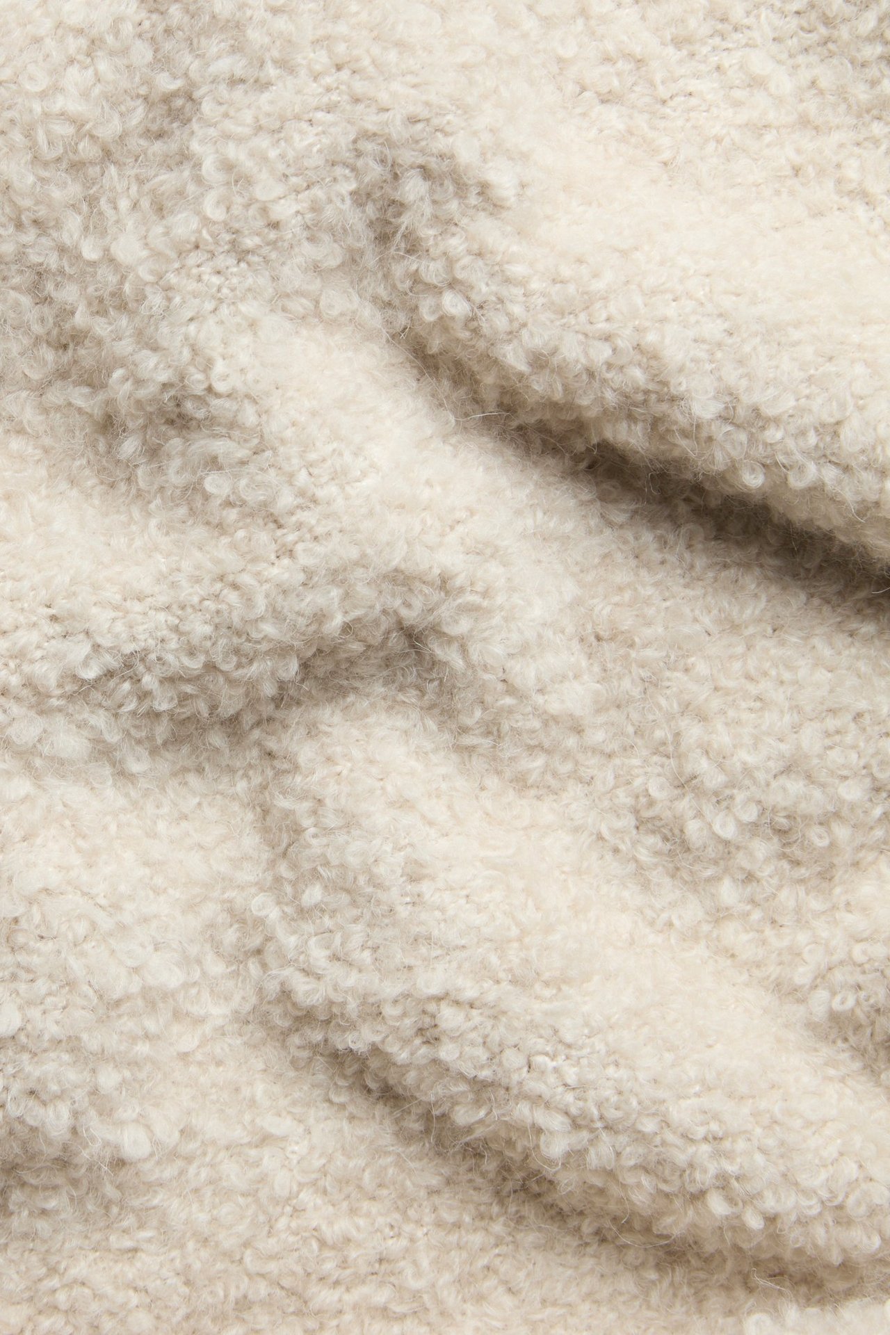 Nærbilde av beige bouclé-strikket genserstoff, som viser dets teksturerte, løkkede overflate og myke folder.