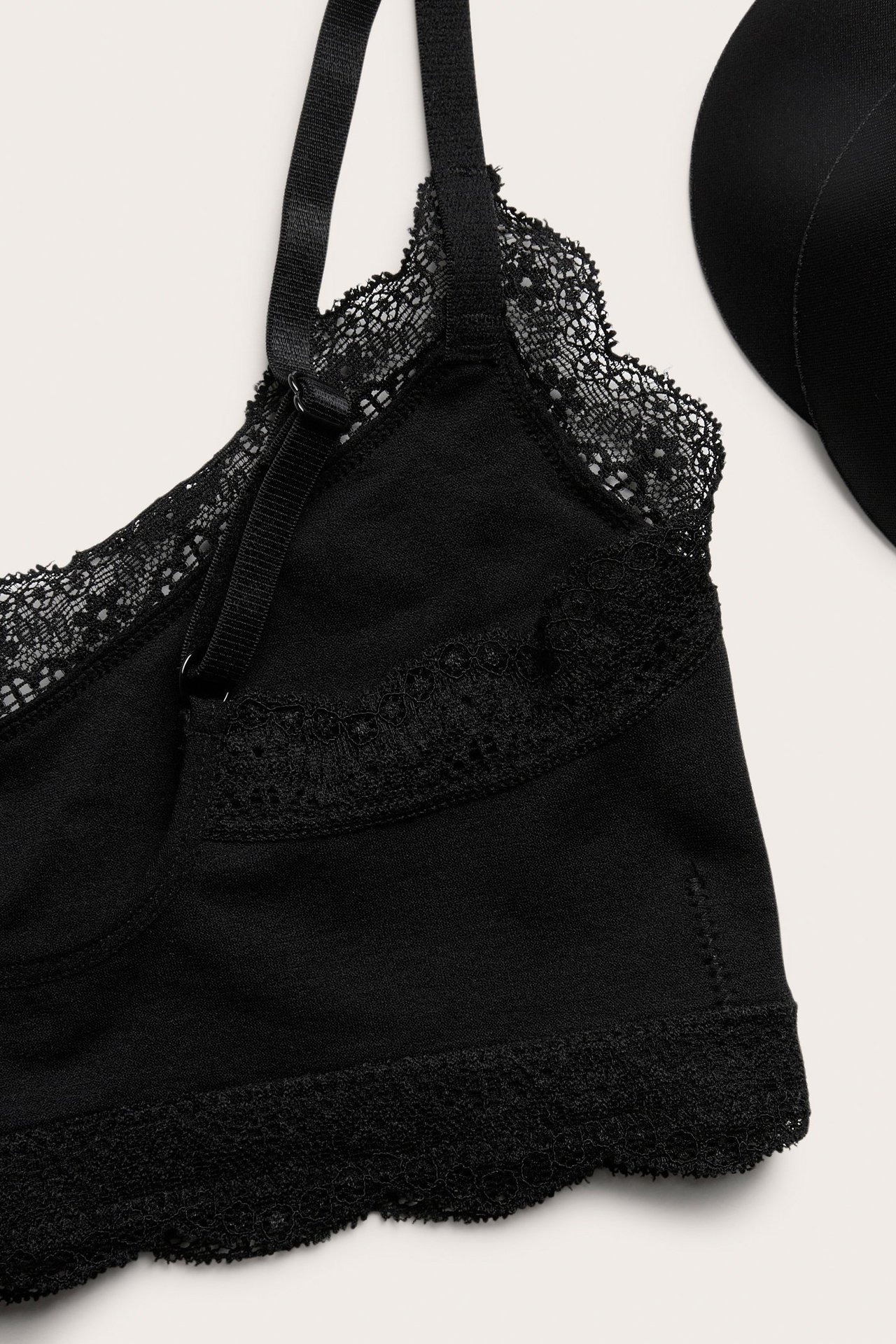 Zbliżenie czarnego biustonosza z koronkowym wykończeniem, regulowanym ramiączkiem i czarną wyjmowaną wkładką.