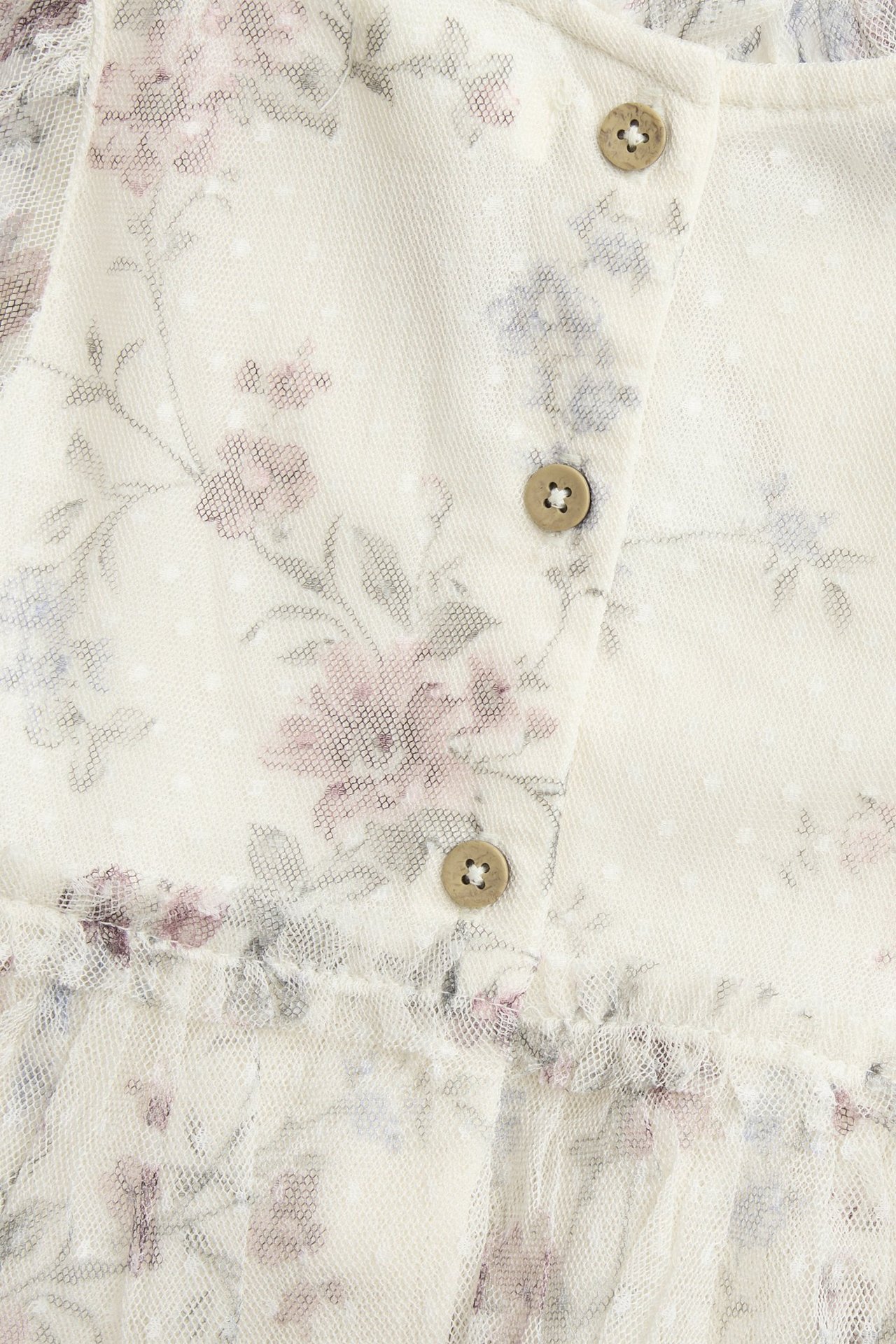 Zbliżenie na jasnobeżową kwiecistą sukienkę z siateczki z kropkowaną teksturą i trzema jasnobrązowymi guzikami.