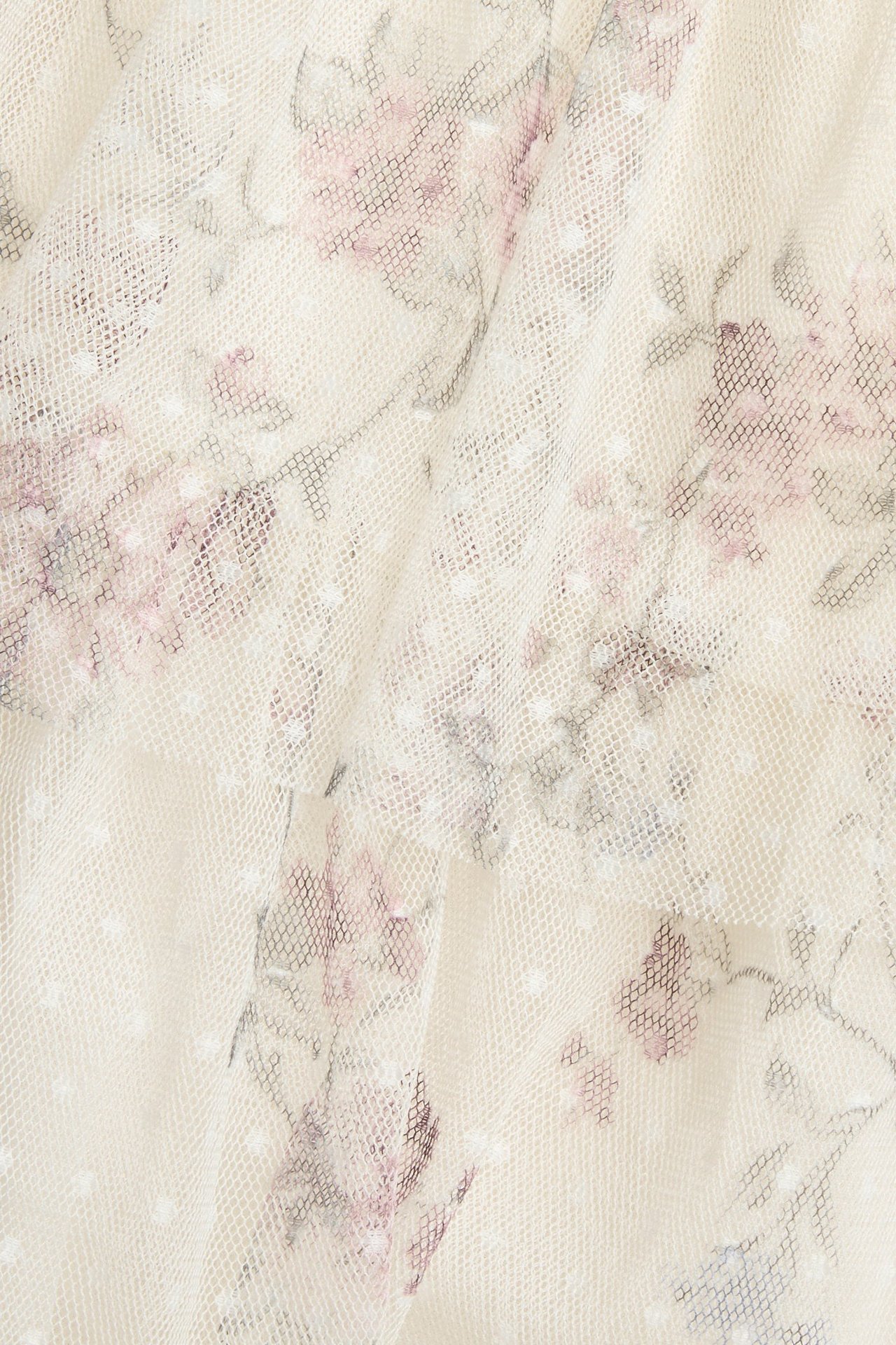 Zbliżenie jasnobeżowej siateczkowej tkaniny w kwiaty, z małymi białymi kropkami i różowymi kwiatami.