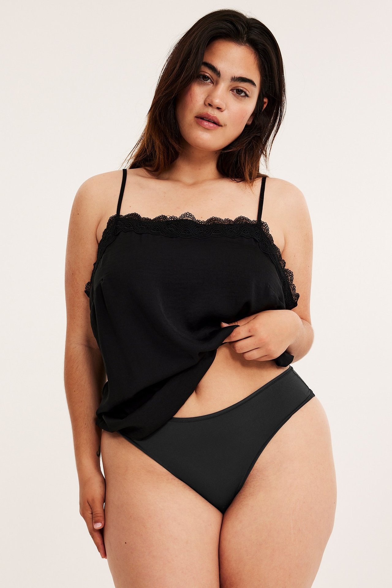 Forfra, kvinne i svarte høytlivs stringtruser og svart blondekantet camisole.