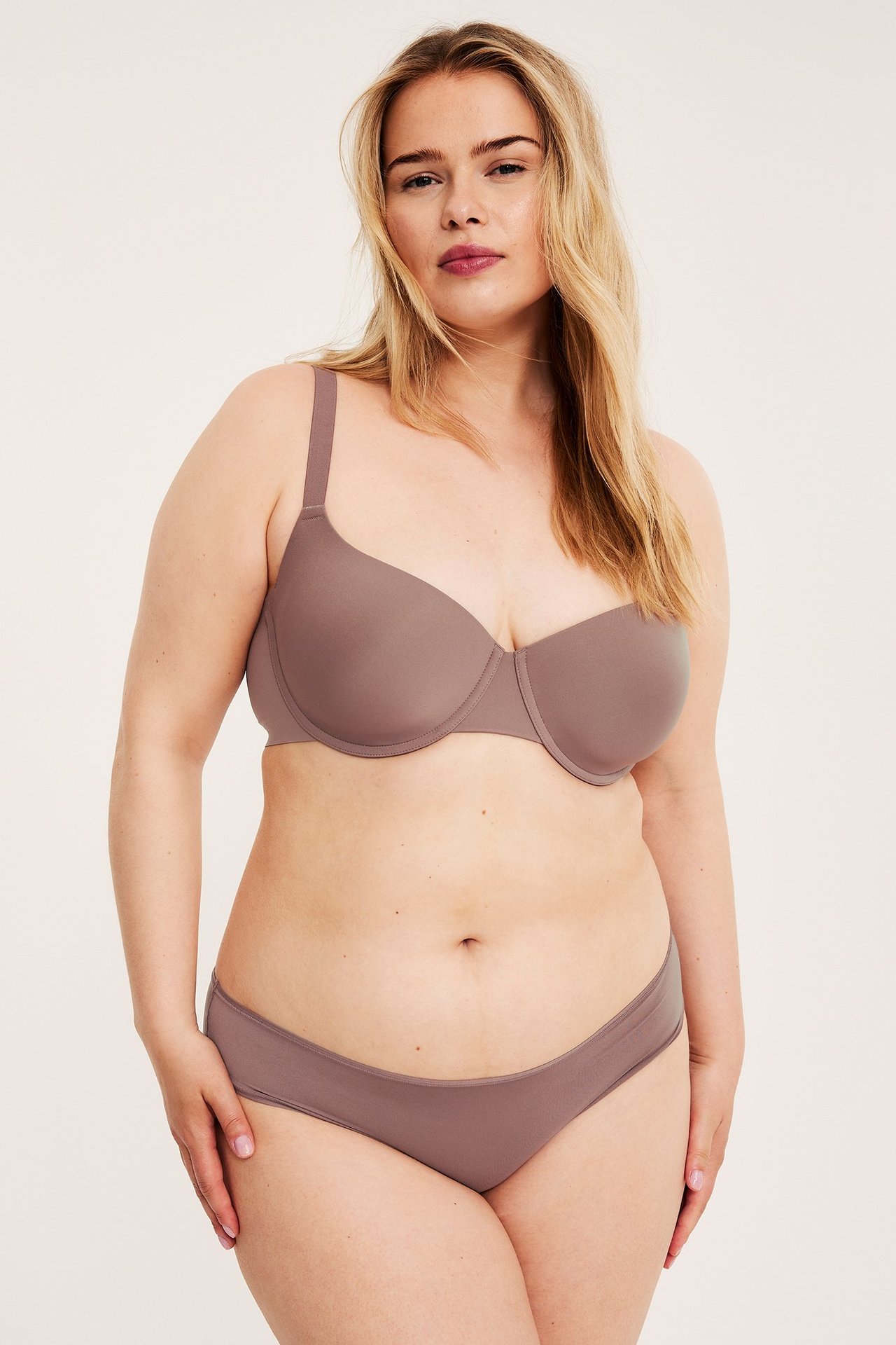Forfra, kvinne i ensfargede støvrosa stringtruser med høyt liv og matchende BH.