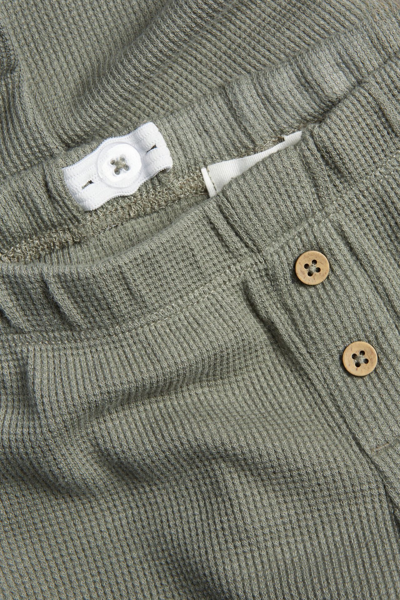 Zbliżenie na ciemnozielone waflowe legginsy dziecięce, z regulowaną gumką i drewnianymi guzikami.