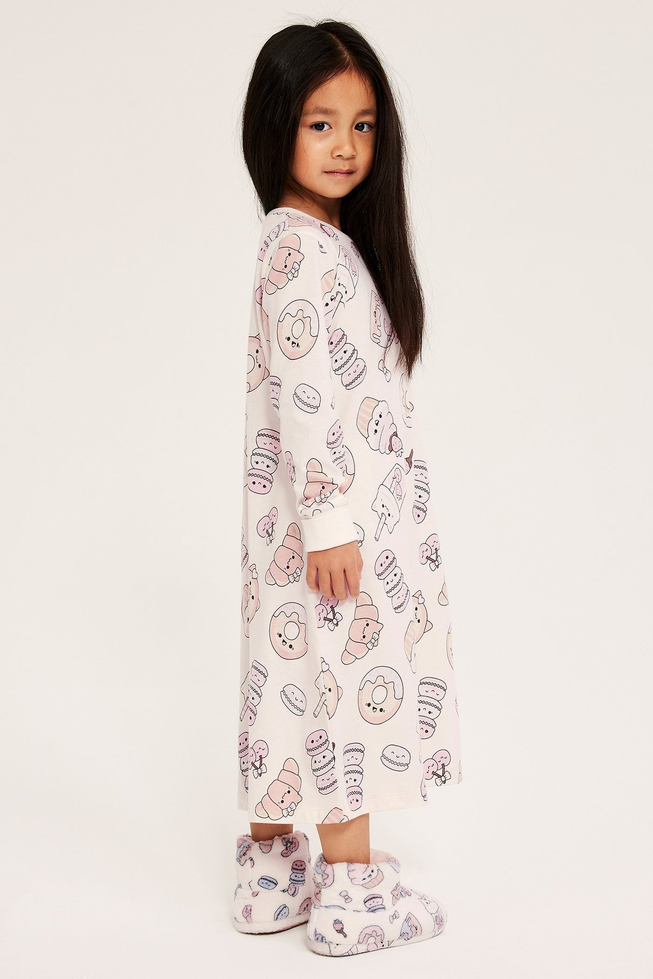 Sivukuva lapsesta valkoisessa puuvillayöpaidassa, jossa on makeiskuvio ja siihen sopivat tossut.