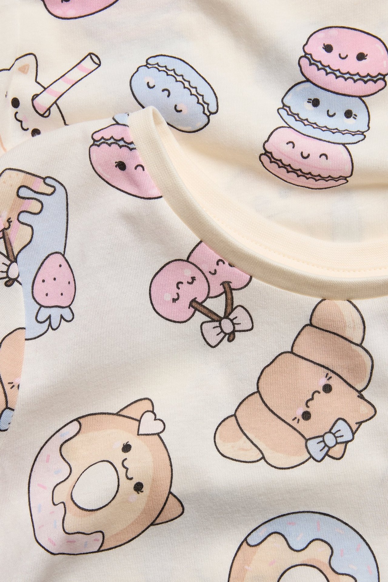 Lähikuva luonnonvalkoisesta puuvillaisesta yöpaidasta, jossa on söpö jälkiruokakuvio.