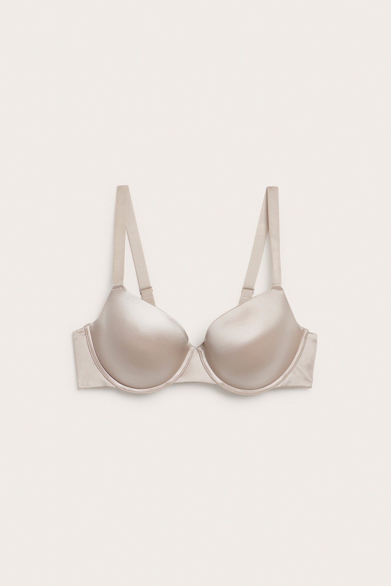 Framifrån, en ljusbeige push up-bh med släta, glansiga kupor och justerbara axelband.