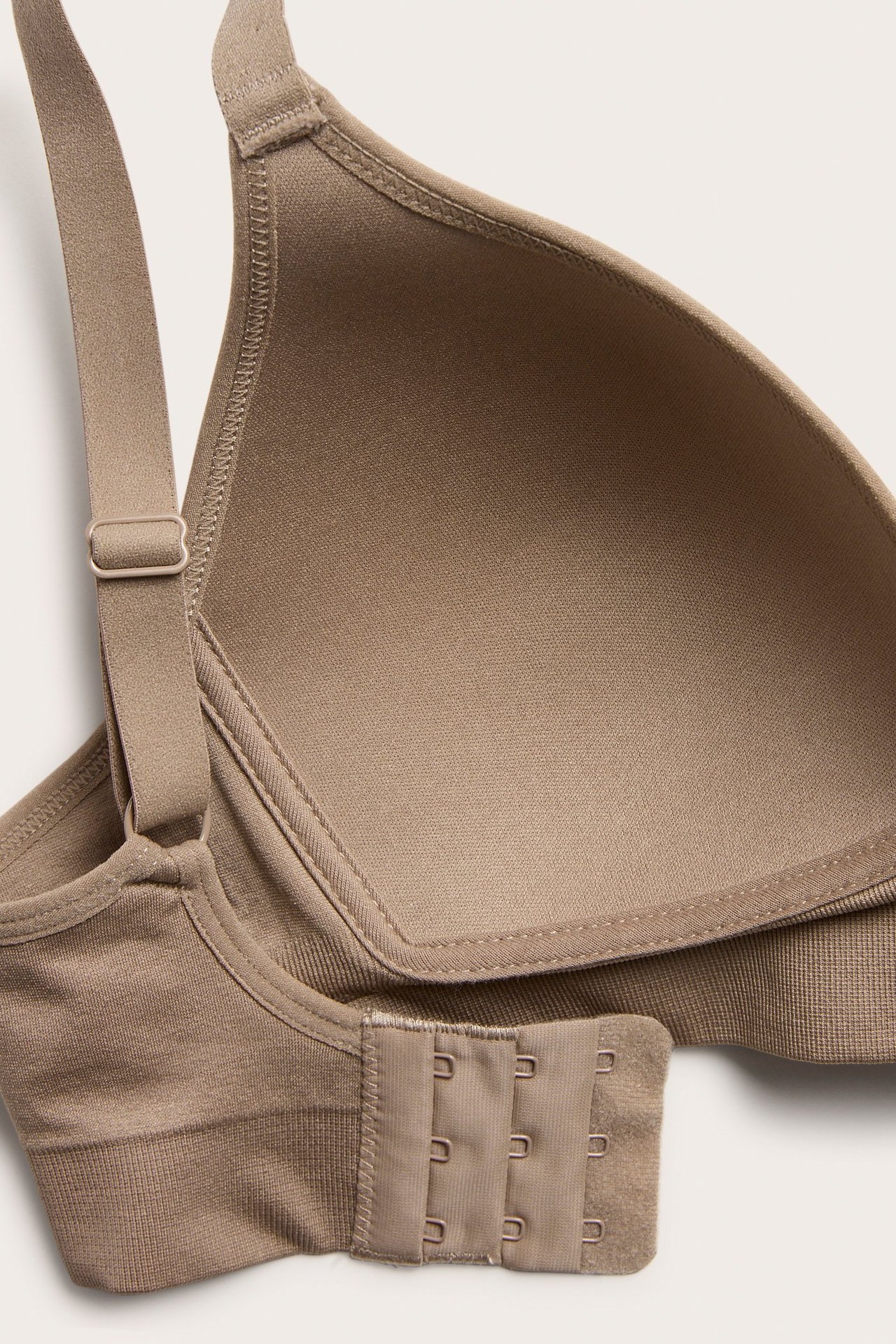 Zbliżenie beżowego, bezszwowego biustonosza bez fiszbin z formowaną miseczką, regulowanym ramiączkiem i zapięciem na haftki.