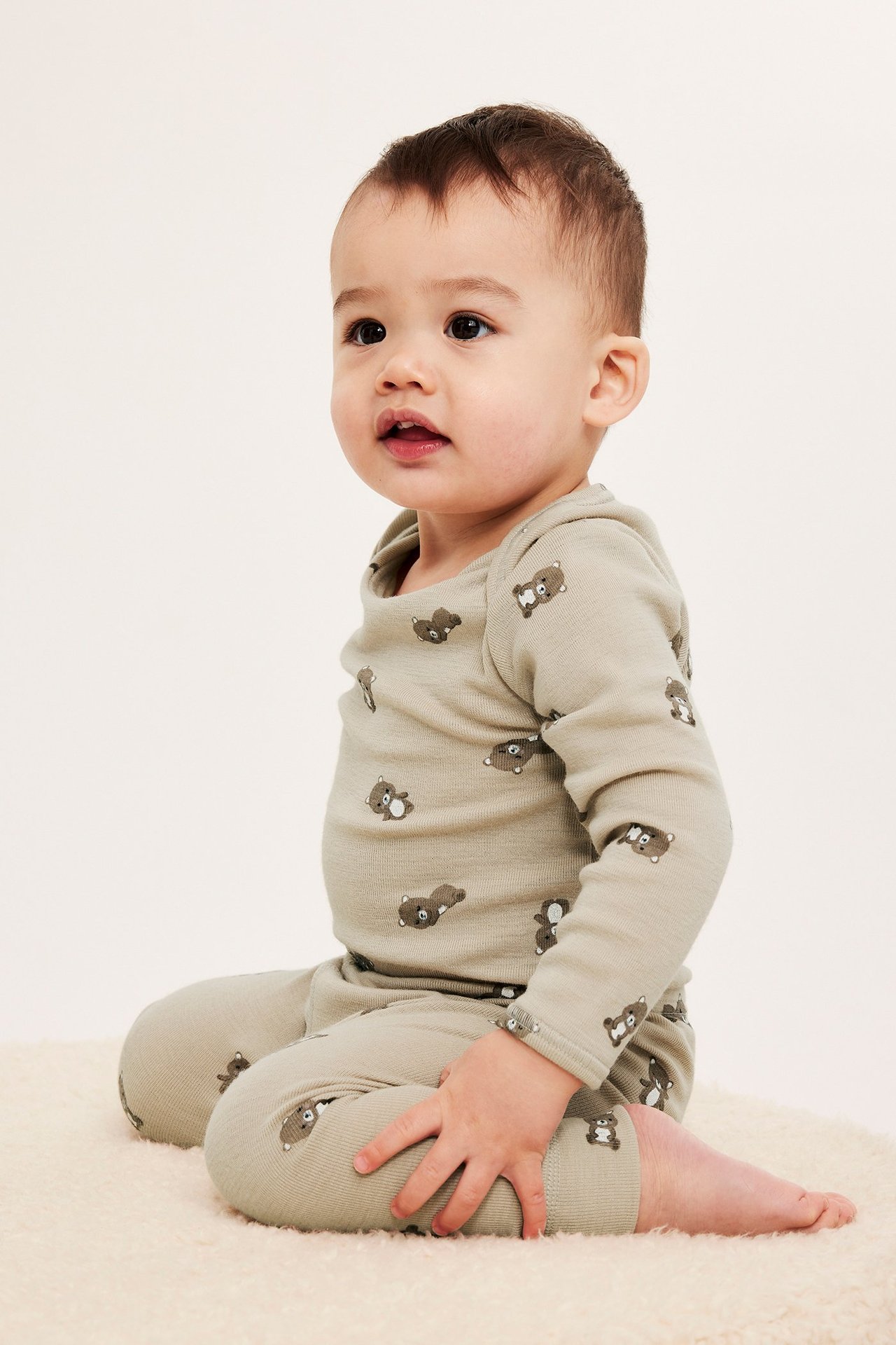 Sivukuva vauvasta yllään beigenvärinen merinovillainen body ja yhteensopivat karhukuvioiset leggingsit.