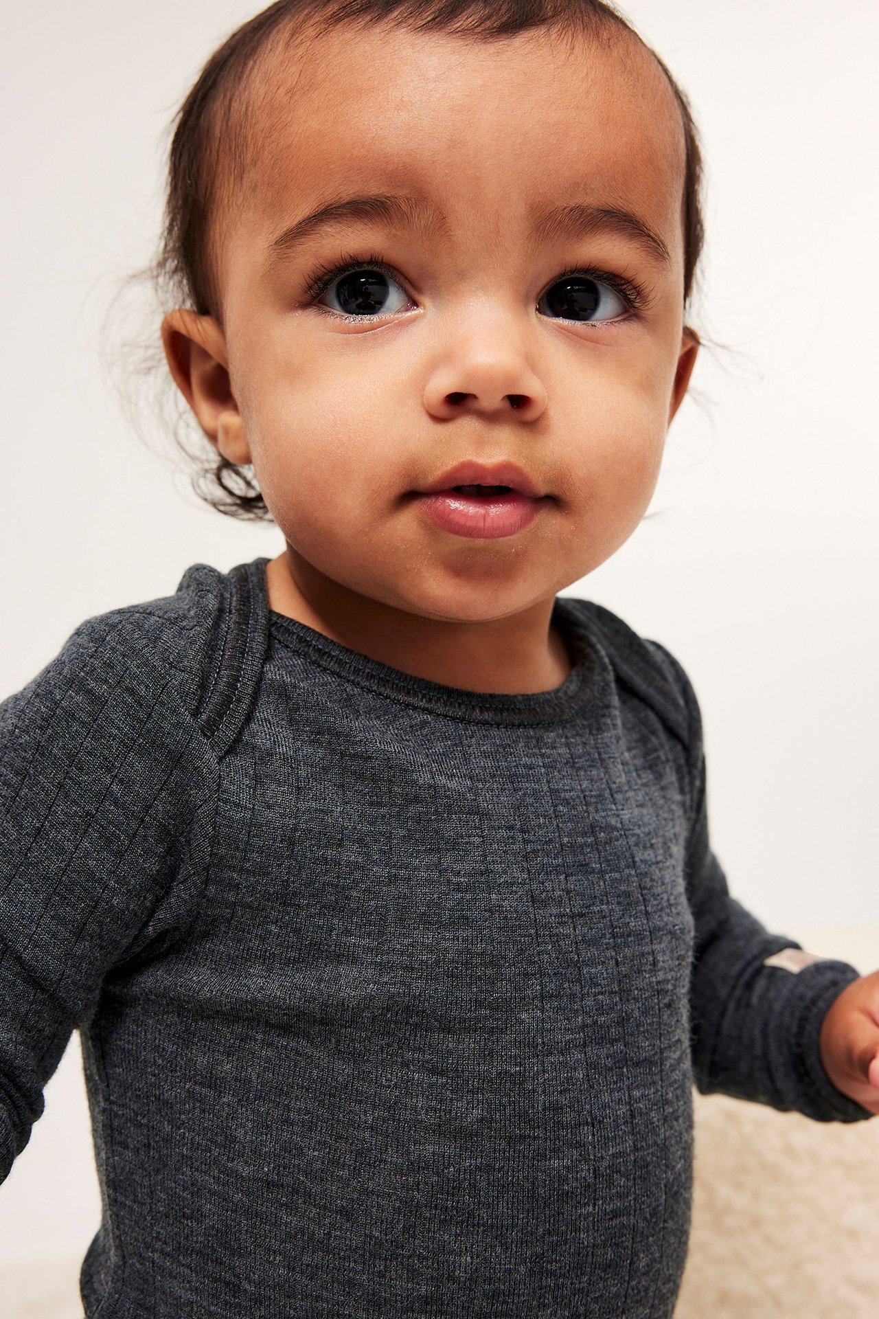 Lähikuva edestä vauvasta yllään harmaa meleerattu ribattu pitkähihainen villabody.