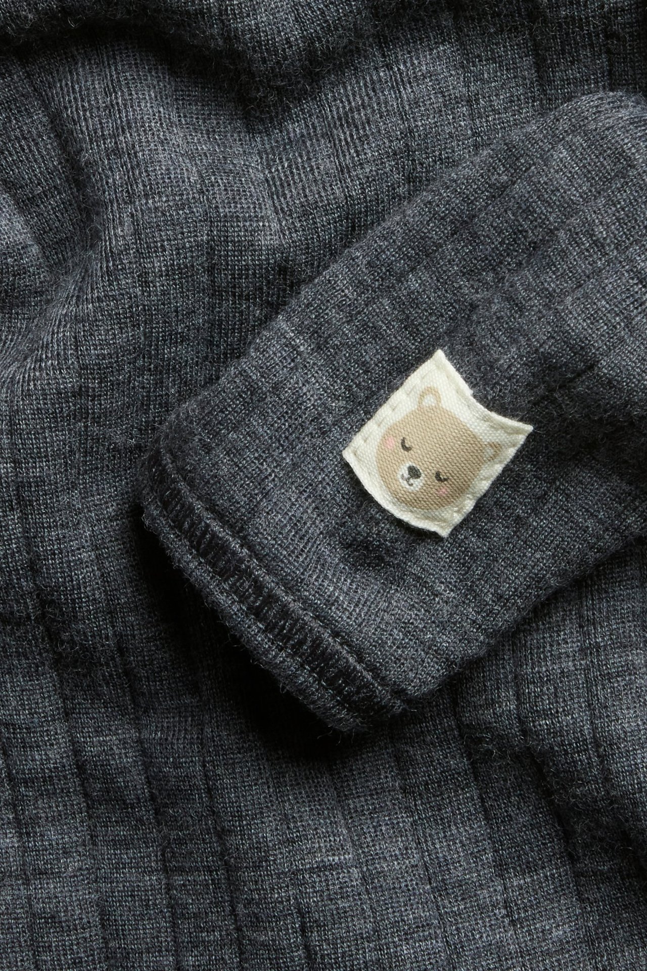 Zbliżenie szarego melanżowego prążkowanego body niemowlęcego z wełny z naszywką misia na rękawie.