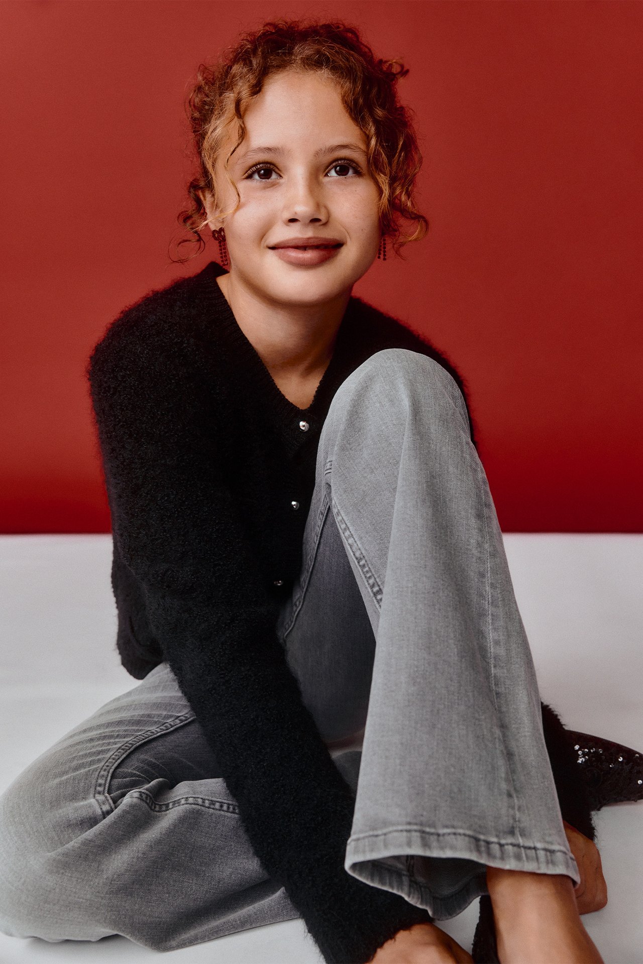 Forfra: Barn i sort bouclé strikket cardigan med metallknapper og grå jeans.