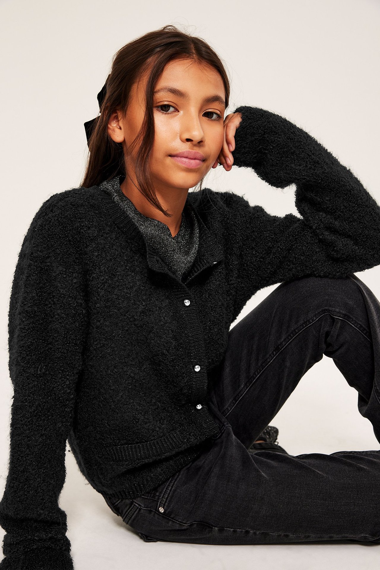 Lapsi yllään musta bouclékardigaani hopeanapeilla, harmaa toppi, mustat farkut ja musta hiusrusetti.