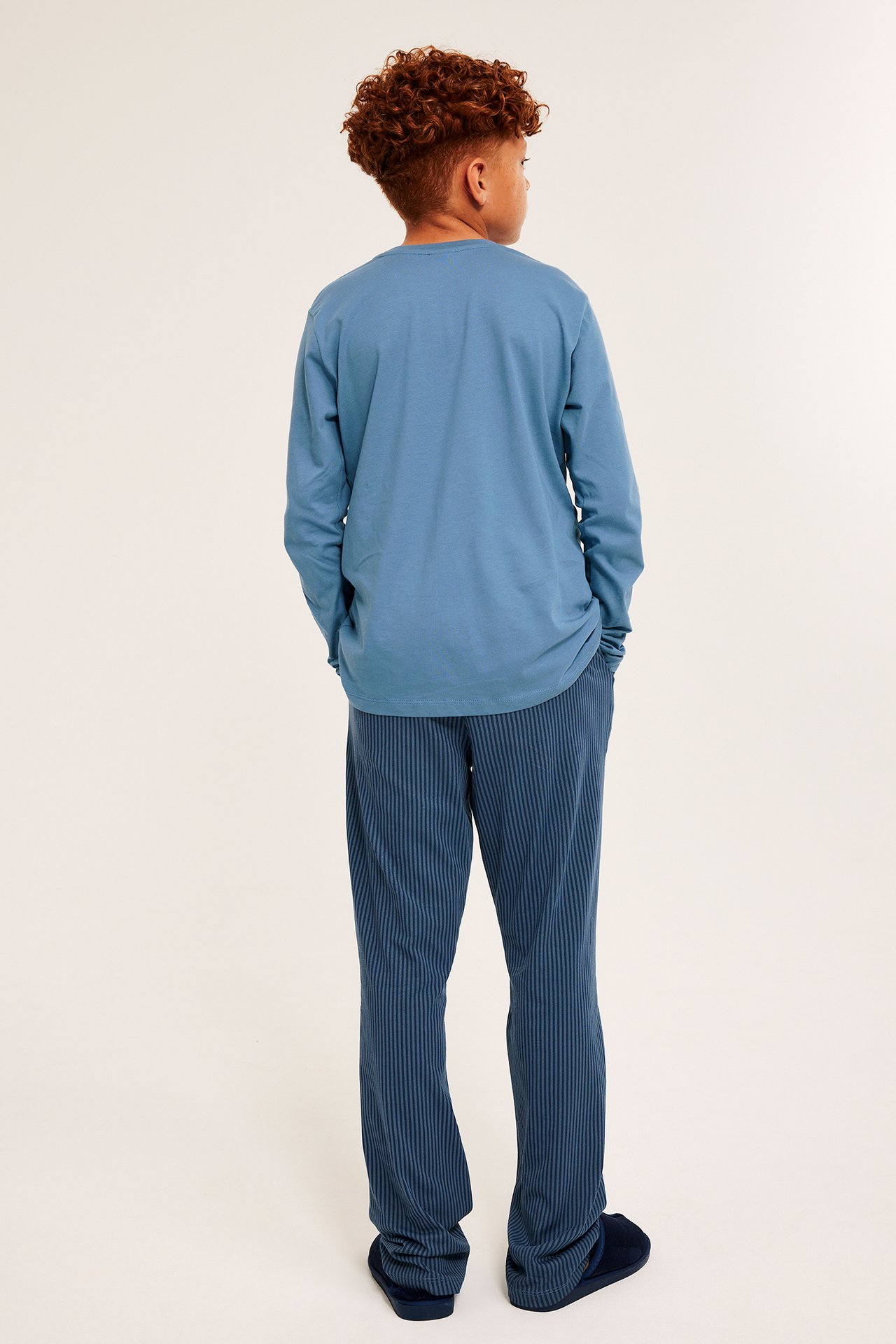 Lapsen selkä, yllään sininen puuvillainen pitkähihainen pyjamatop ja uurretut tummansiniset pyjamahousut.