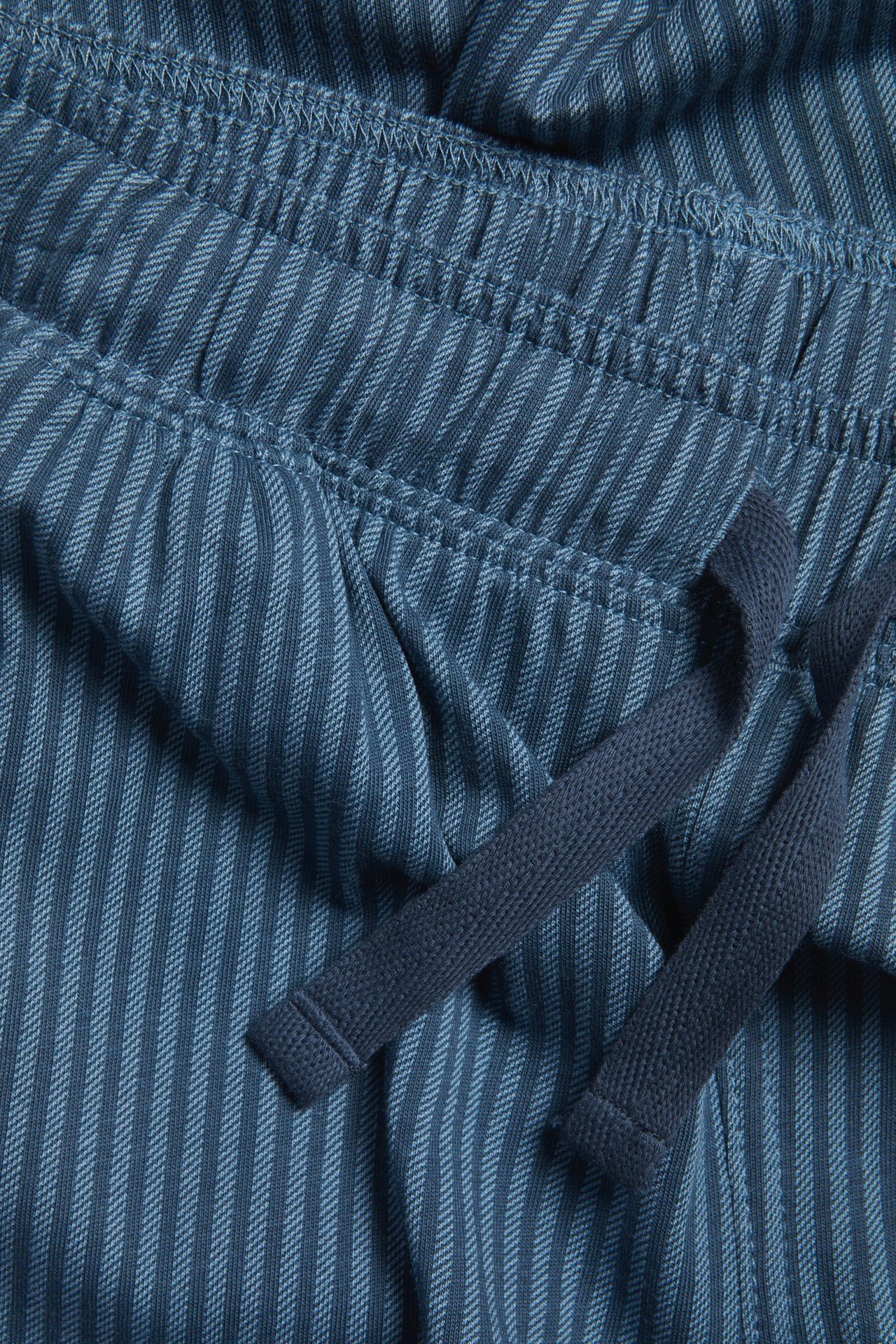 Zbliżenie niebieskich bawełnianych spodni od piżamy z elastycznym, pasiastym pasem i sznurkiem.