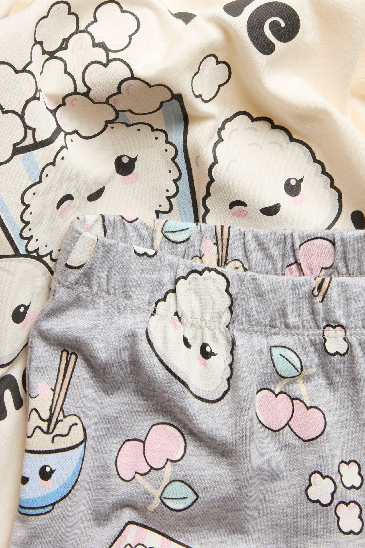Zbliżenie na dziecięcą piżamę: kremowy bawełniany top z nadrukiem chmury i szare wzorzyste bawełniane spodnie.