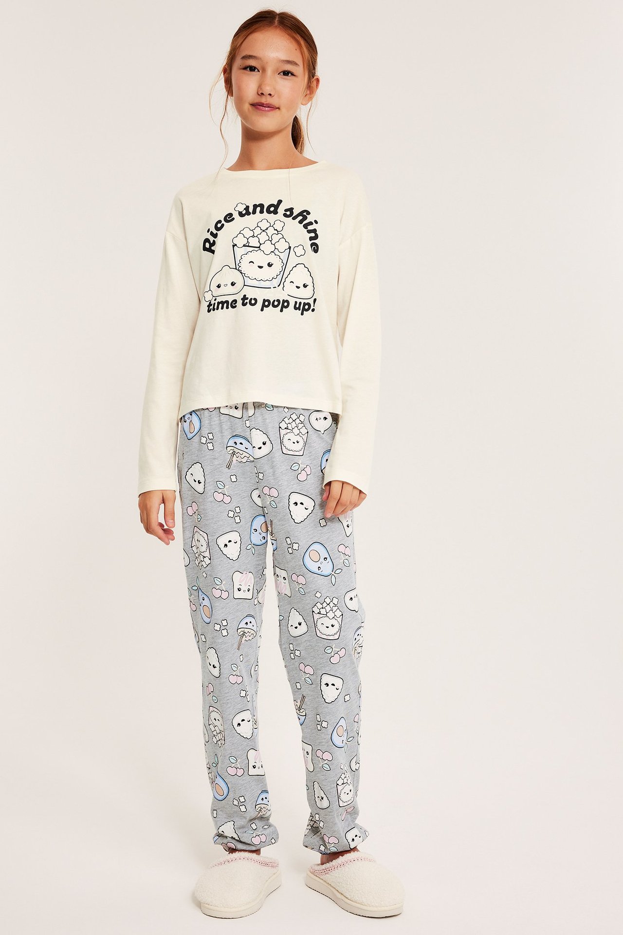 Jente i offwhite pysjamas med trykk, mønstrete bukser og hvite tøfler.