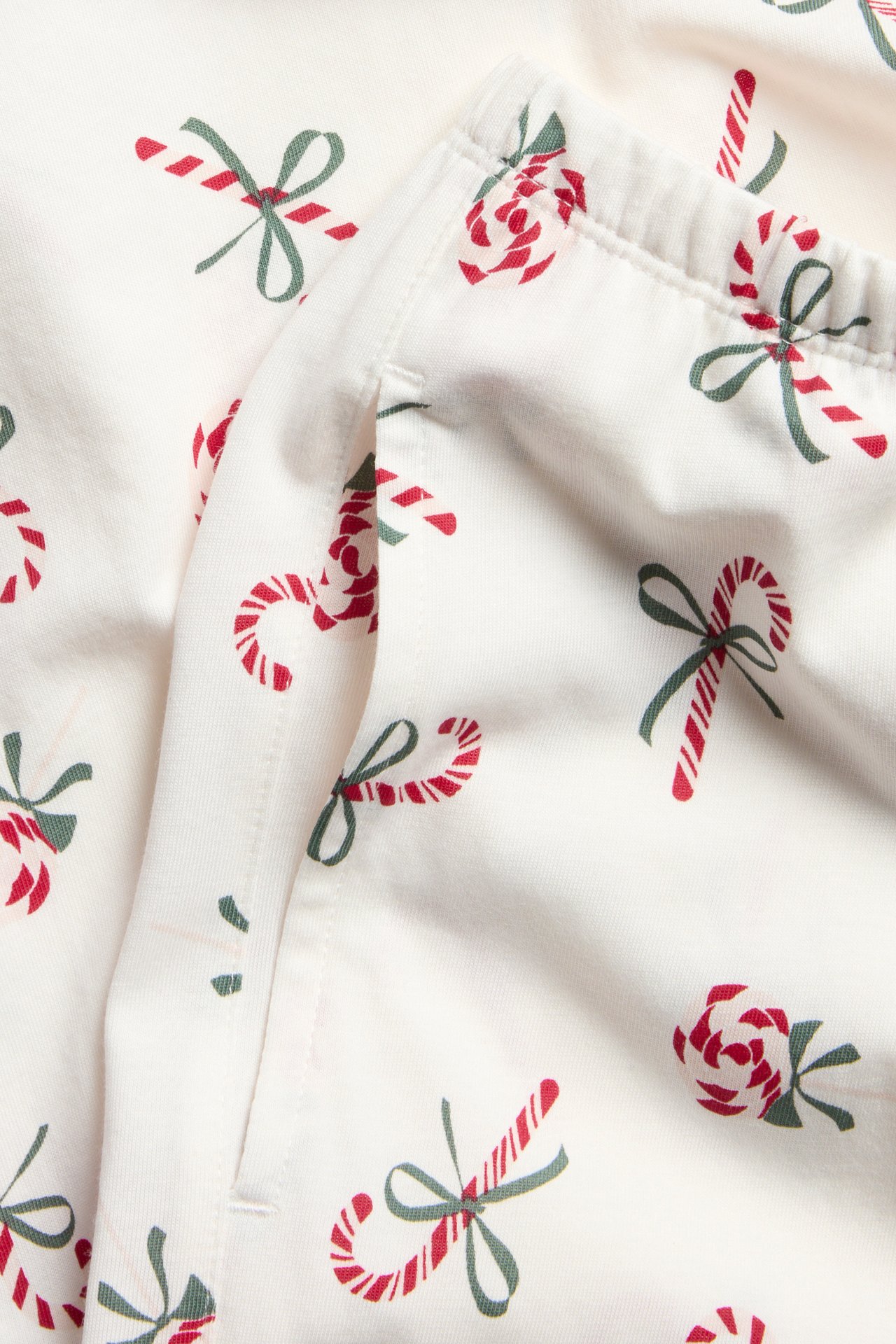 Närbild: vita pyjamasbyxor i bomullstrikå med rött polkagris- och grönt rosettmönster, sidficka.