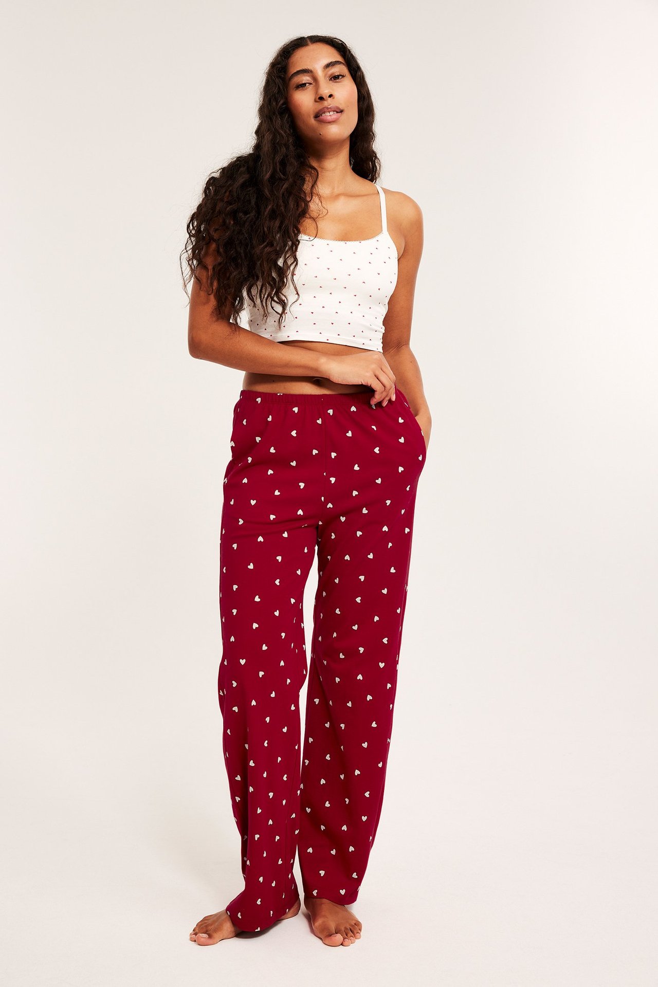 Nainen poseeraa valkoisessa toppi ja punaisissa kuvioiduissa pyjamahousuissa.